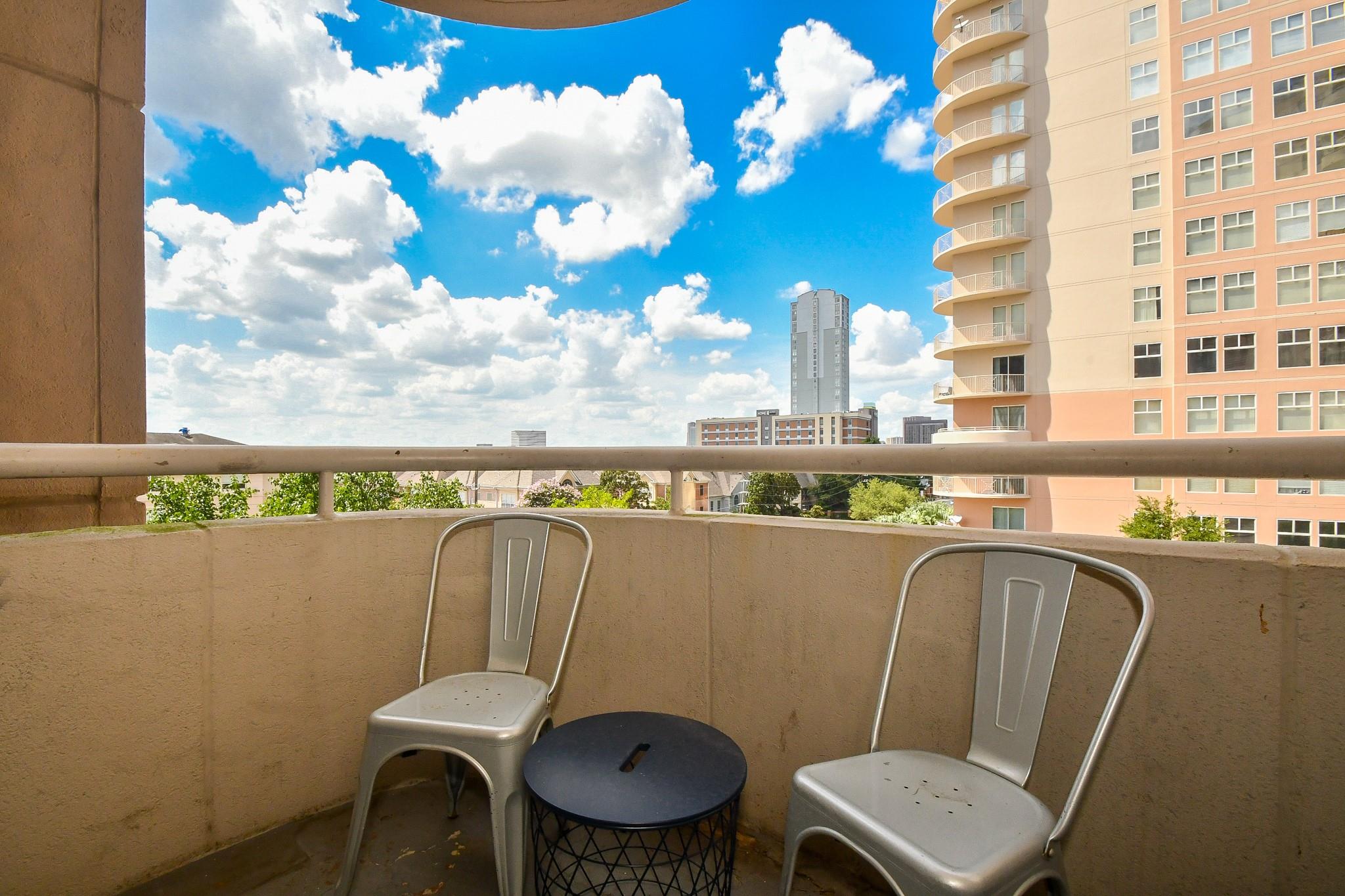 Apartment balcony with two metal chairs and a table overlooking nearby high-rises and the city skyline.