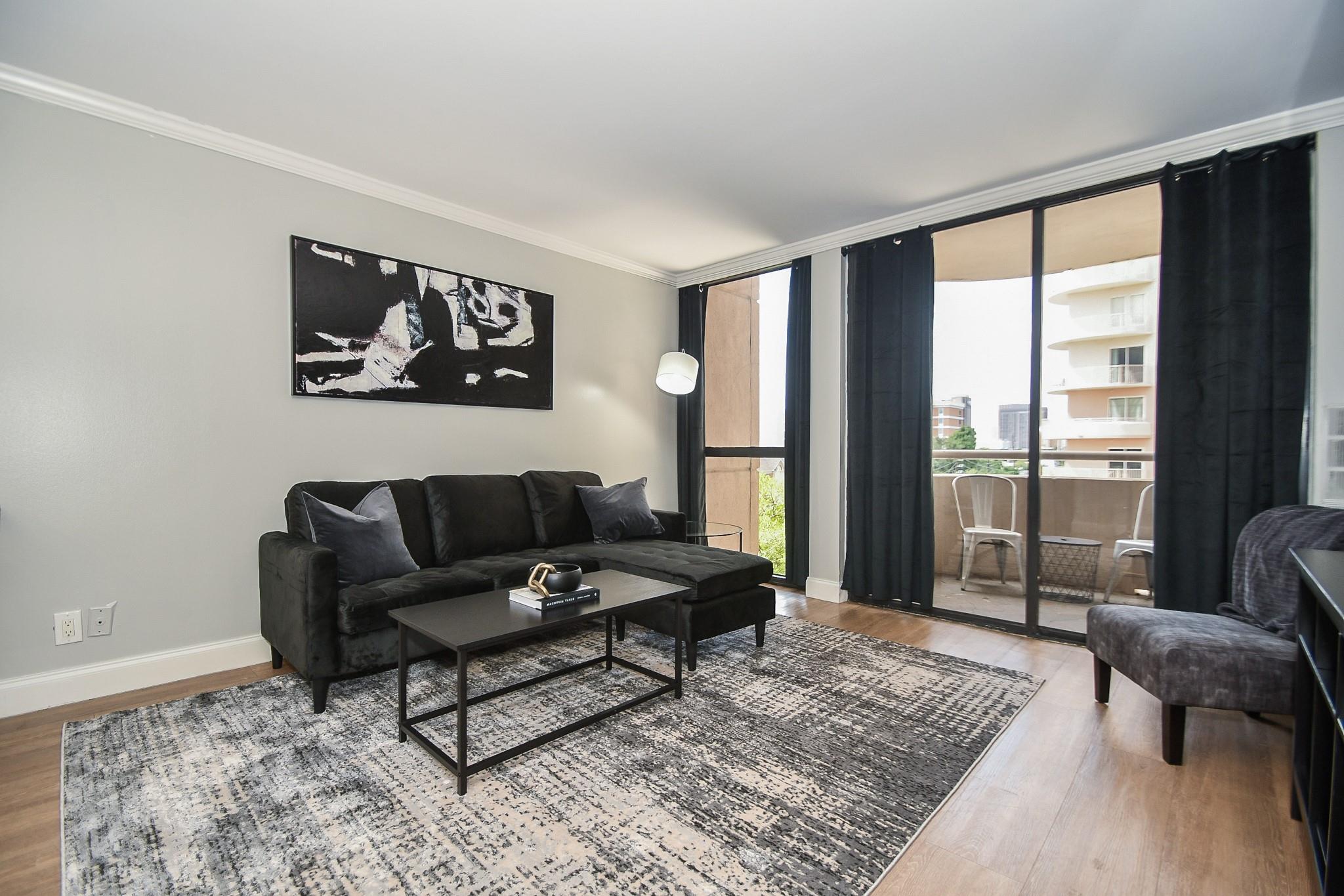 Furnished living room with a black sectional and balcony doors overlooking neighboring buildings.