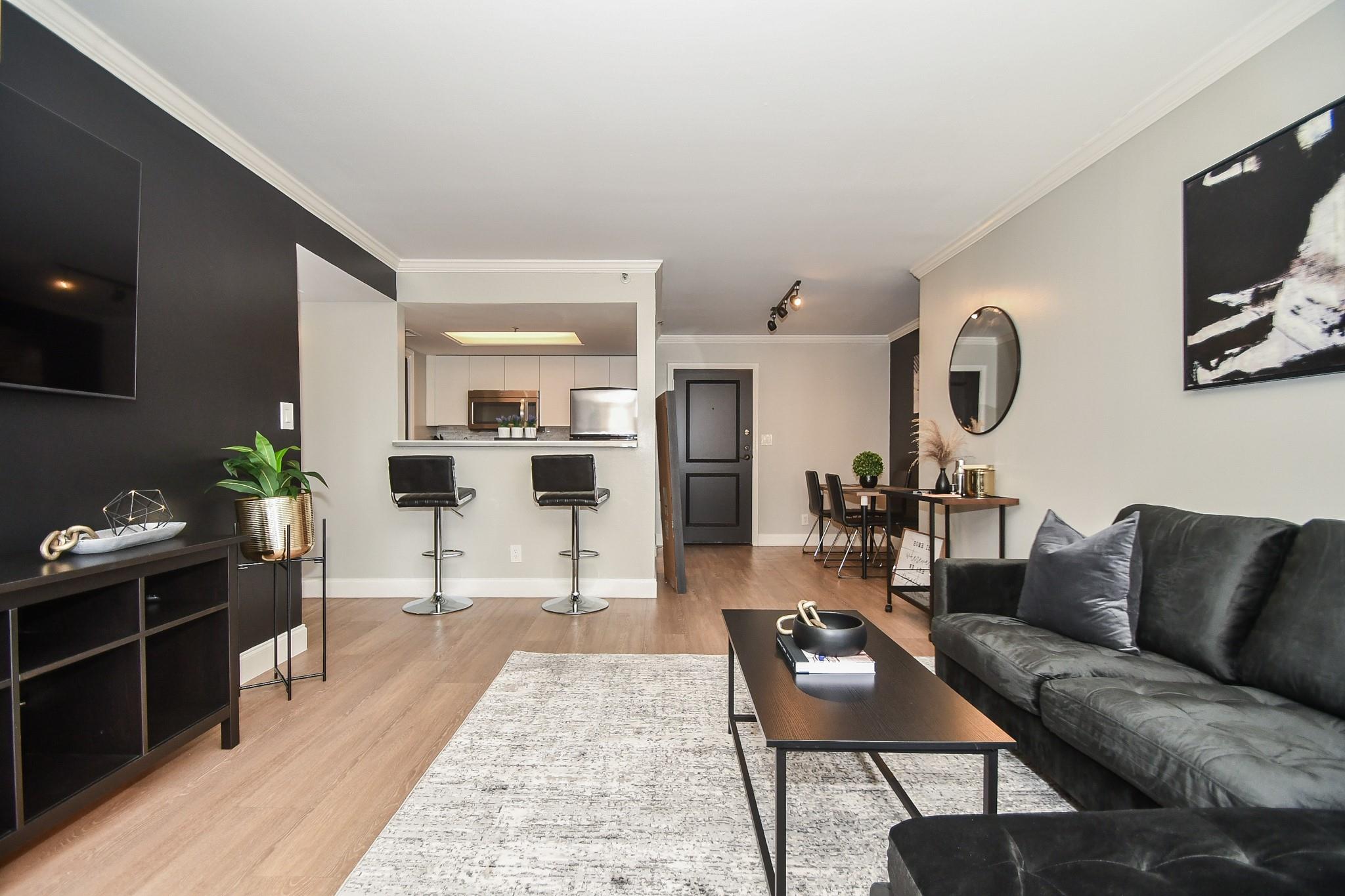 Open-plan condo living room with a charcoal sofa, breakfast bar, and kitchen beyond.
