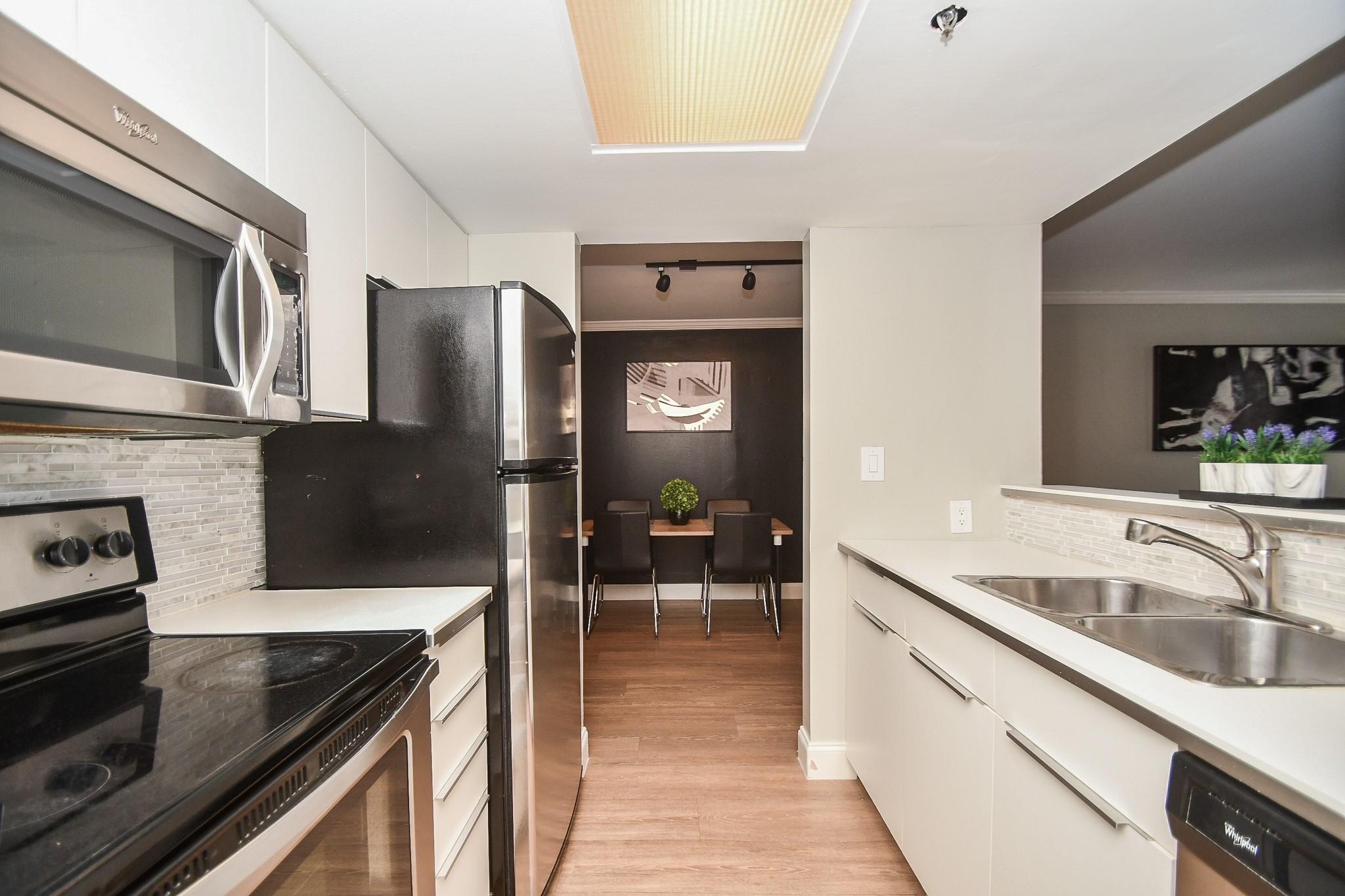 Galley kitchen with stainless steel appliances, white cabinets, and a dining nook at the far end.