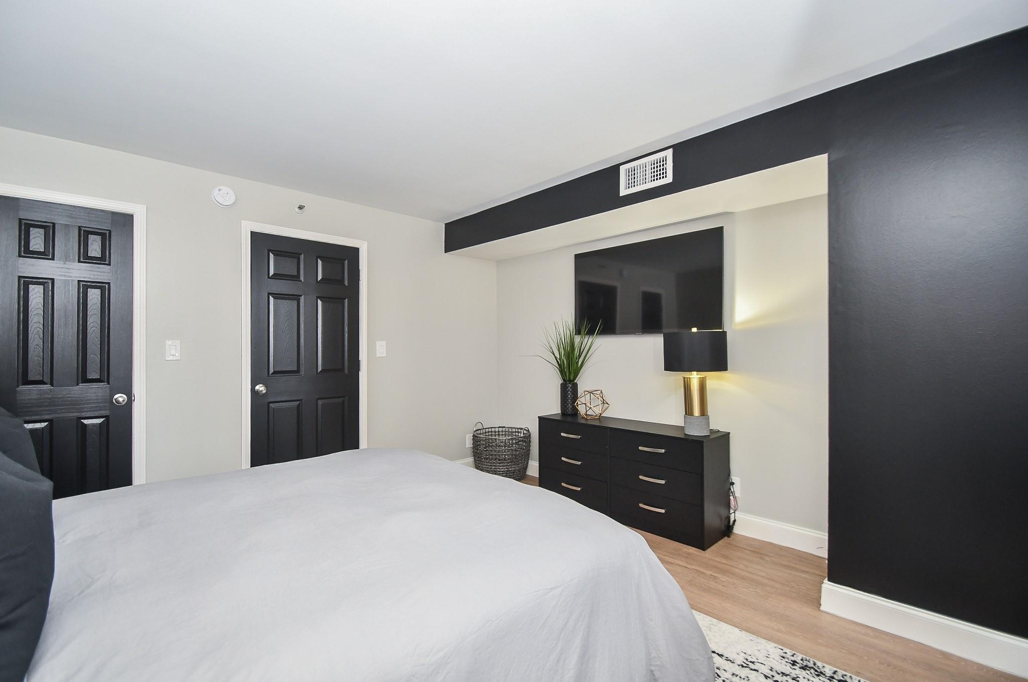 Bedroom with a large bed, black accent wall, and dresser beneath a wall-mounted television.