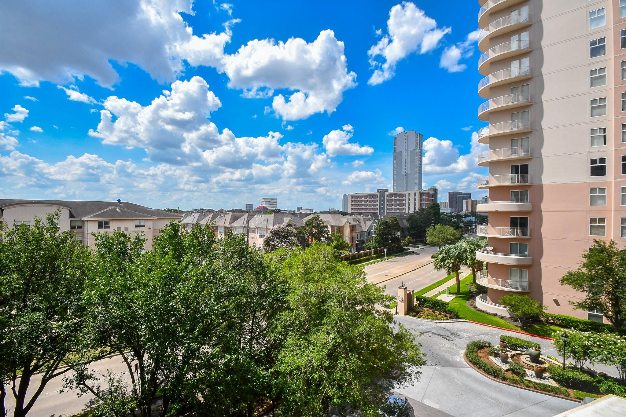 City view from a condominium, with tree-lined streets, nearby homes, and a distant skyline.