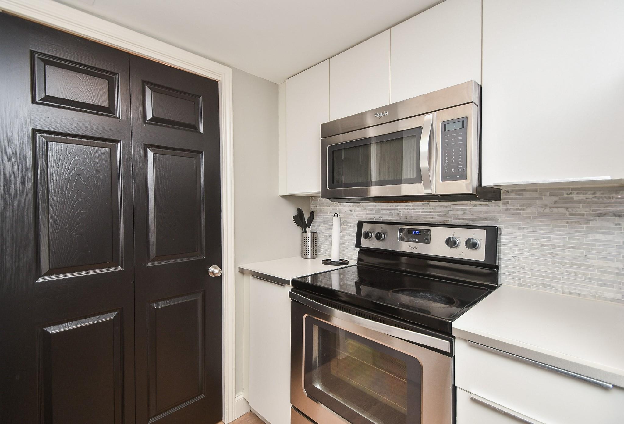 Kitchen with stainless steel appliances, white cabinetry, gray tile backsplash, and dark paneled doors.