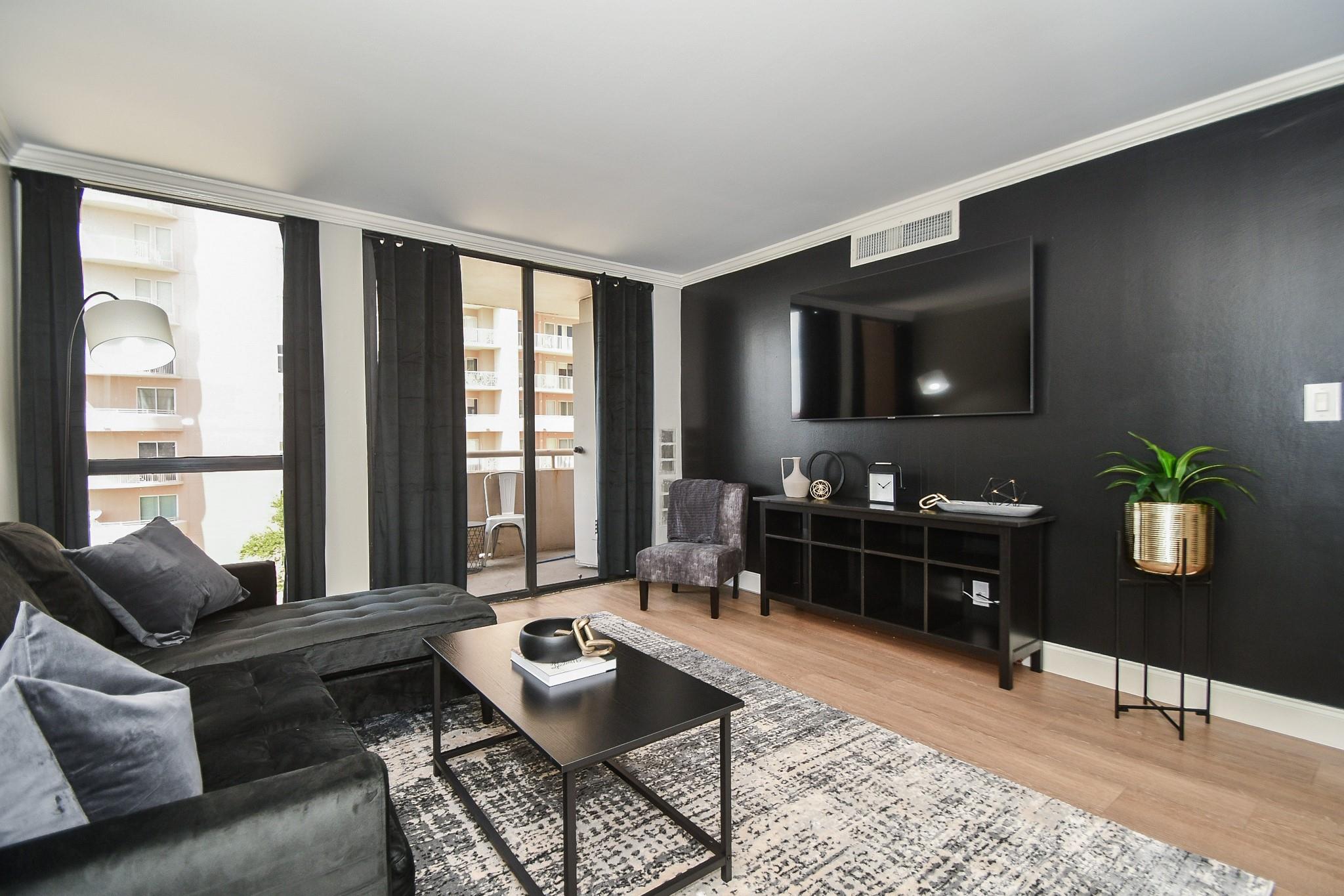 Living room with a charcoal sectional, dark accent wall, mounted television, and balcony doors.