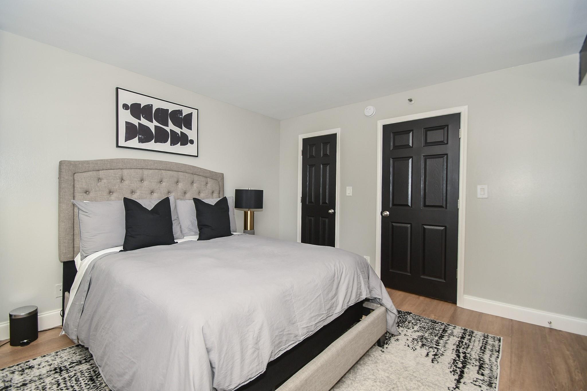 Furnished bedroom with a gray bed, tufted headboard, black accent pillows, and patterned rug.