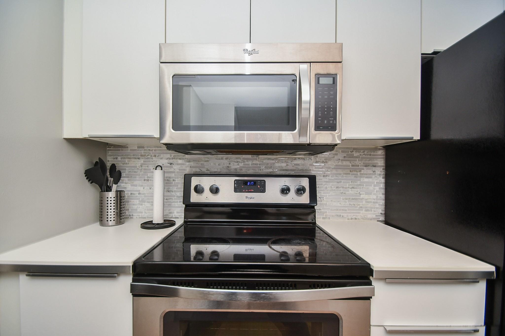 Kitchen range and over-the-range microwave with stainless-steel finishes, white cabinets, and a gray tile backsplash.