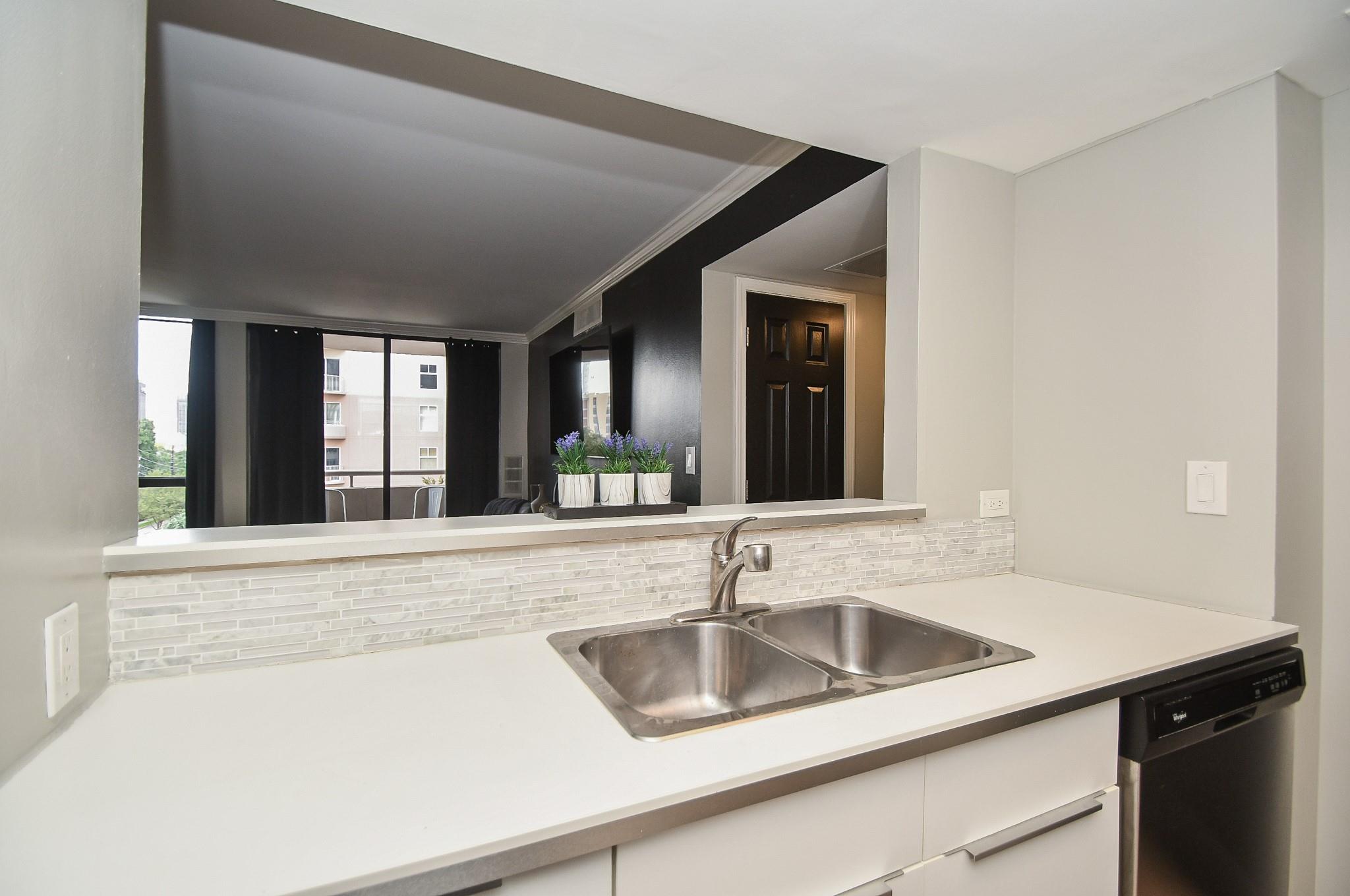 Kitchen with a stainless steel double sink, white counters, and a pass-through to the living area.