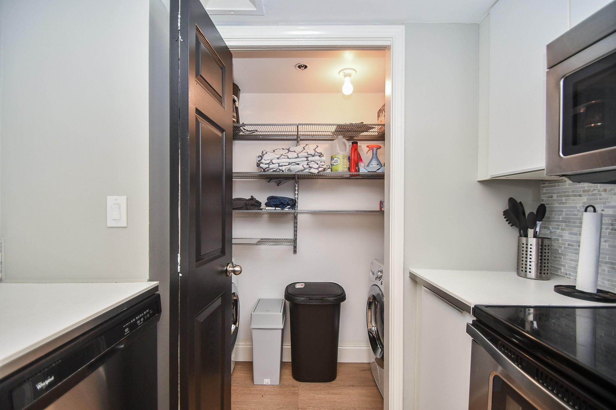 Laundry closet with stacked wire shelves, washer and dryer, and baskets beside the kitchen.