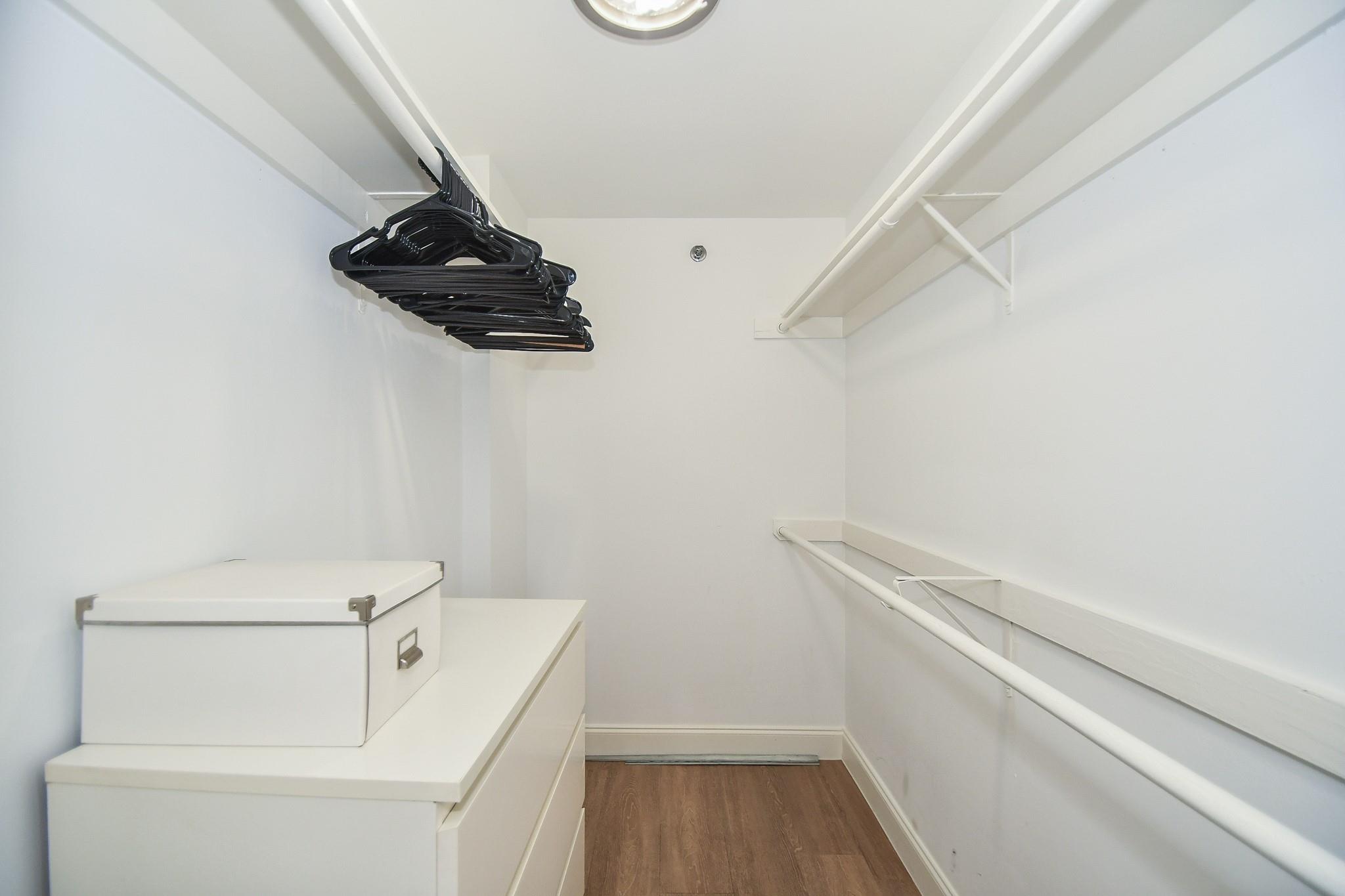 Walk-in closet with hanging rods, black hangers, and white drawers.