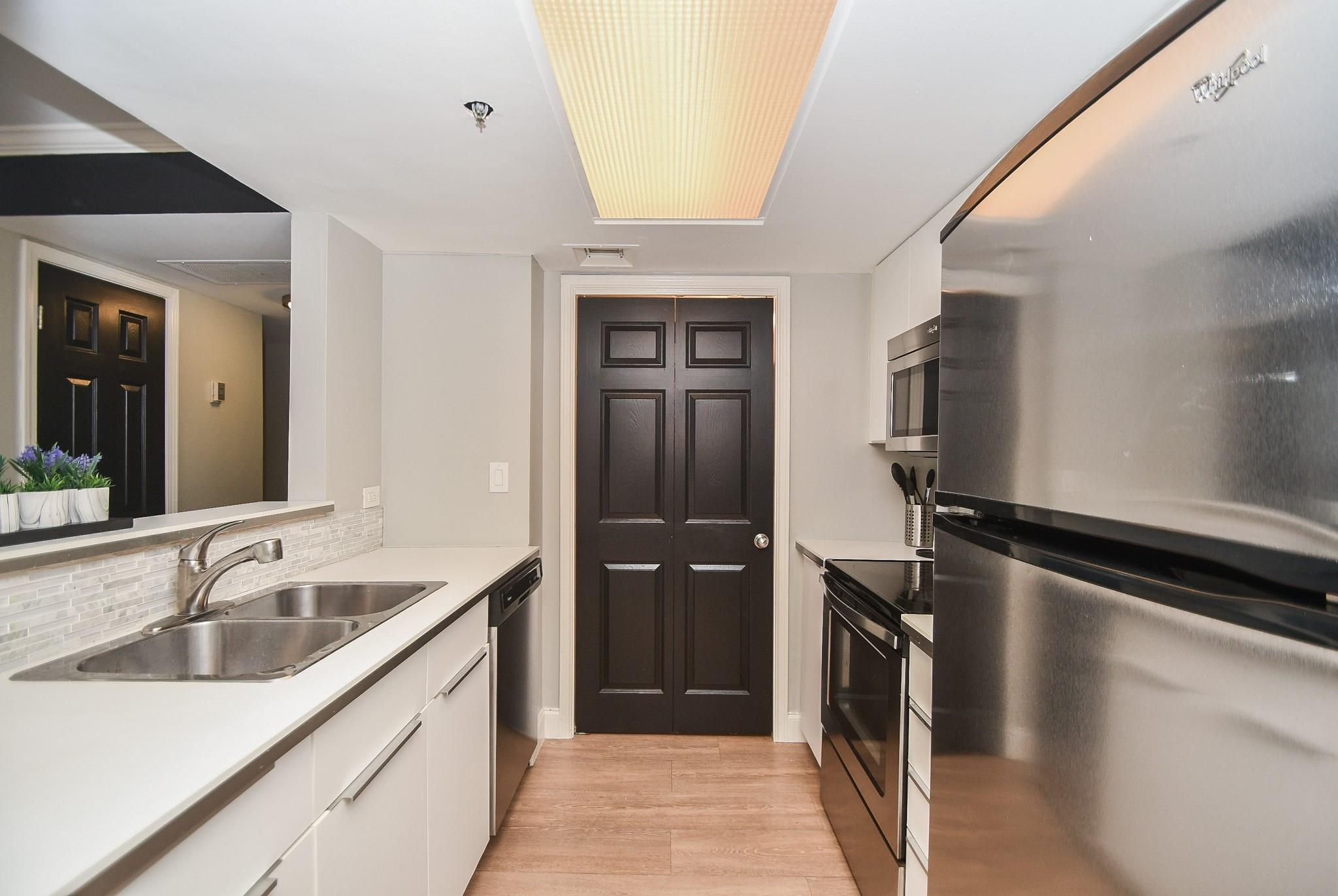 Compact kitchen with white cabinets, double sink, stainless steel appliances, and dark double doors.
