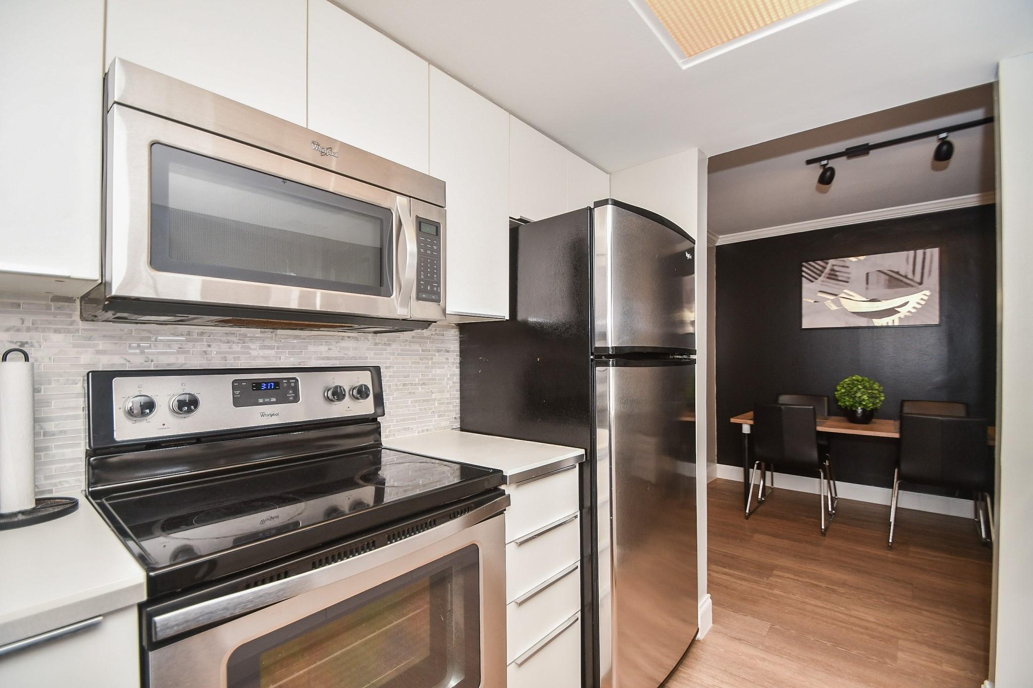 Apartment kitchen with stainless steel appliances and a dining nook with dark walls.
