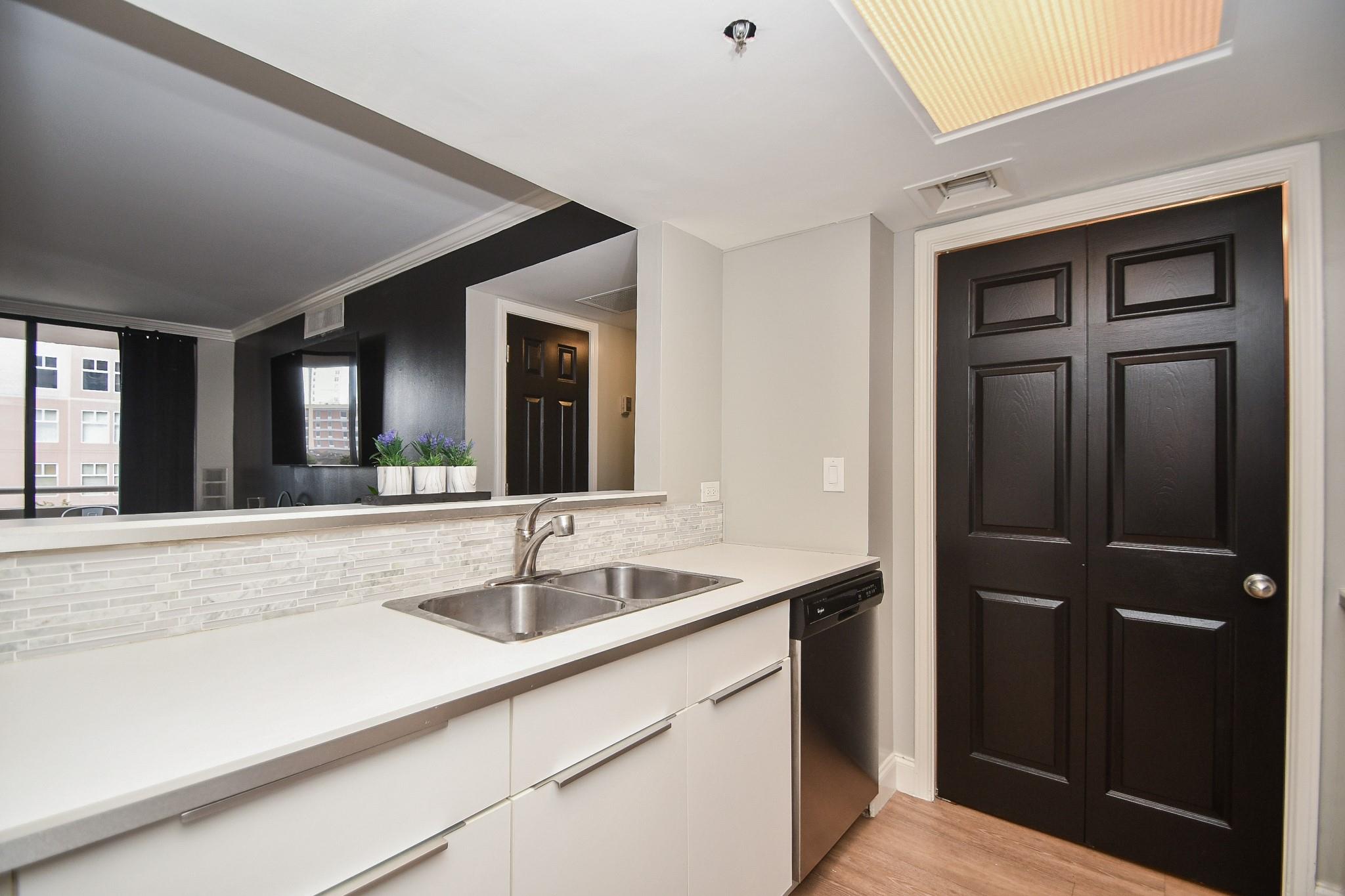 Condo kitchen with a double sink, white counters, pale tile backsplash, and dark paneled doors.