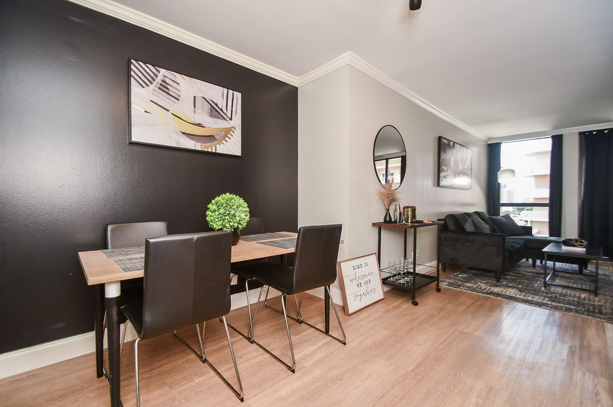 Dining and living room with a wood table, black accent wall, and dark sofa by the window.