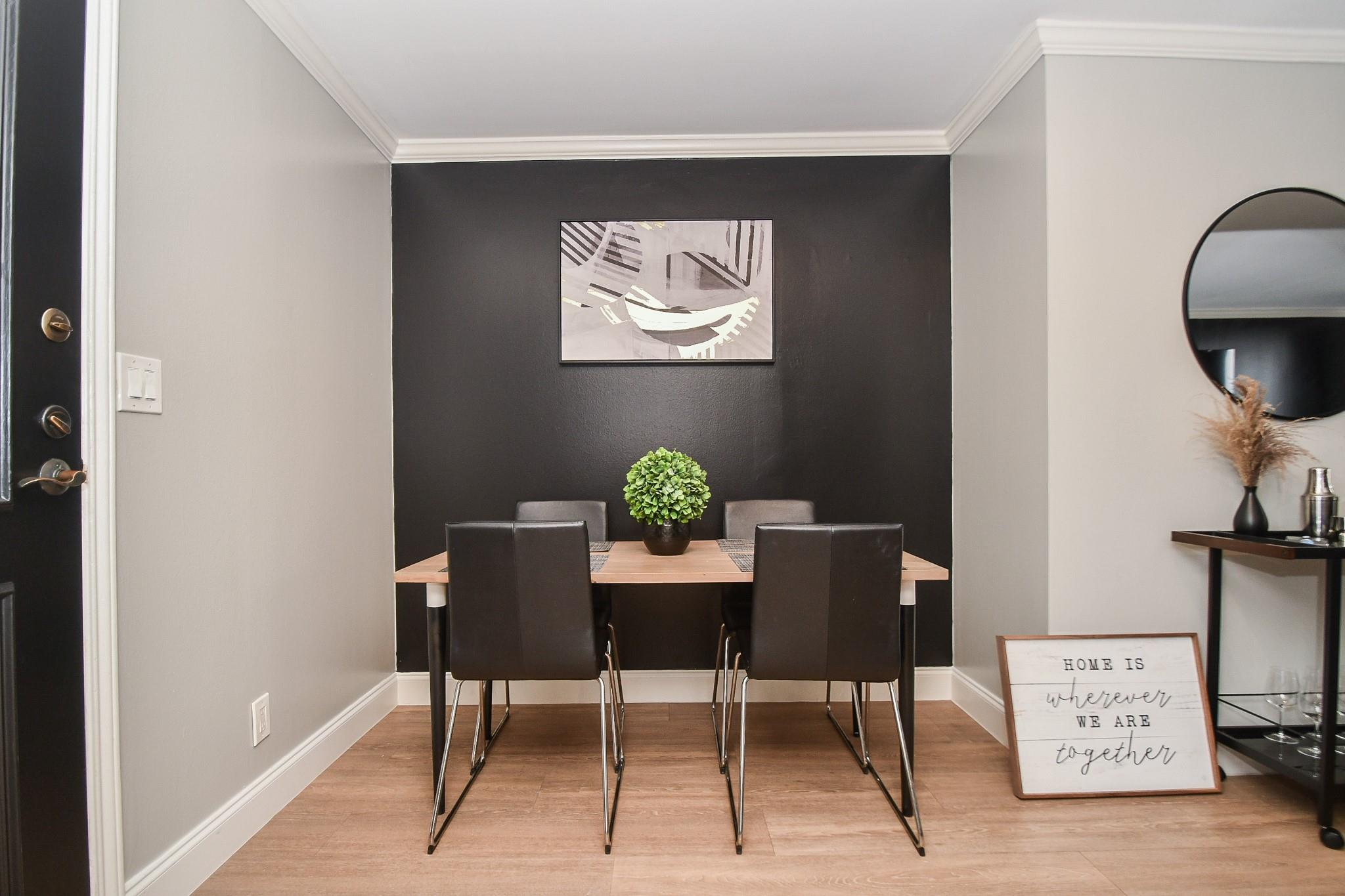 Dining area with a wood table, dark chairs, charcoal accent wall, and framed home sign.