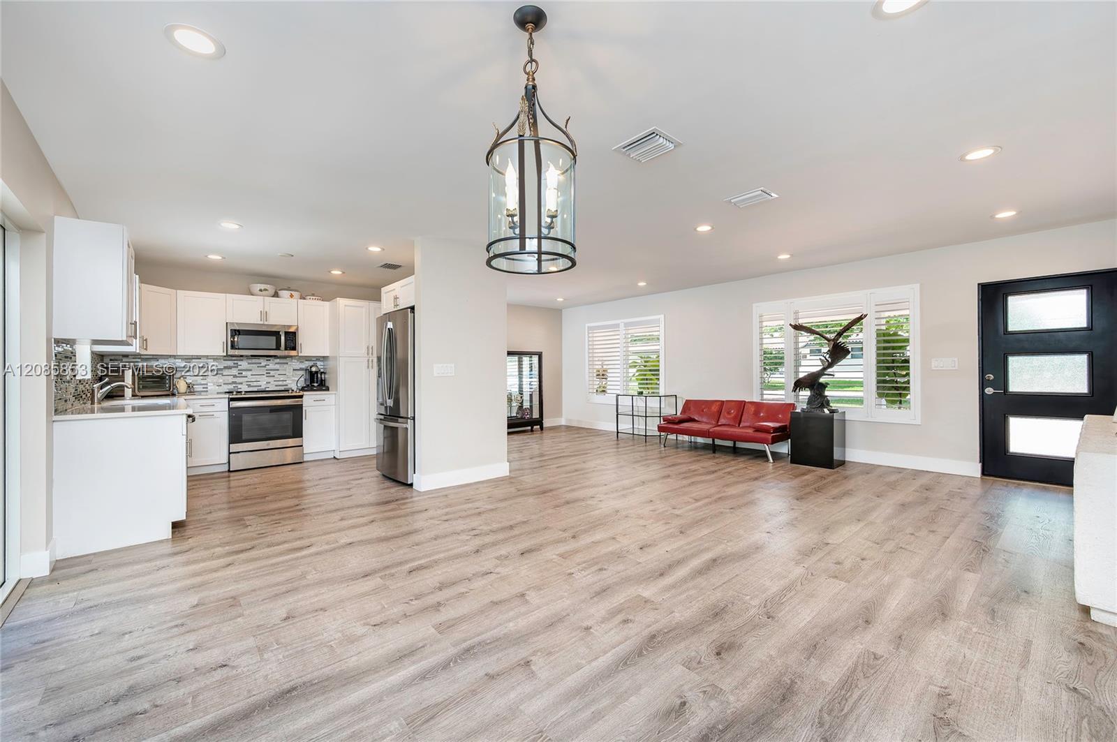 Open-plan kitchen and living room with white cabinetry, light wood-look floors, and a red leather sofa.