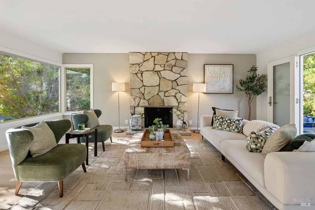 Furnished living room with a prominent stone fireplace, bay windows, and green accent chairs.