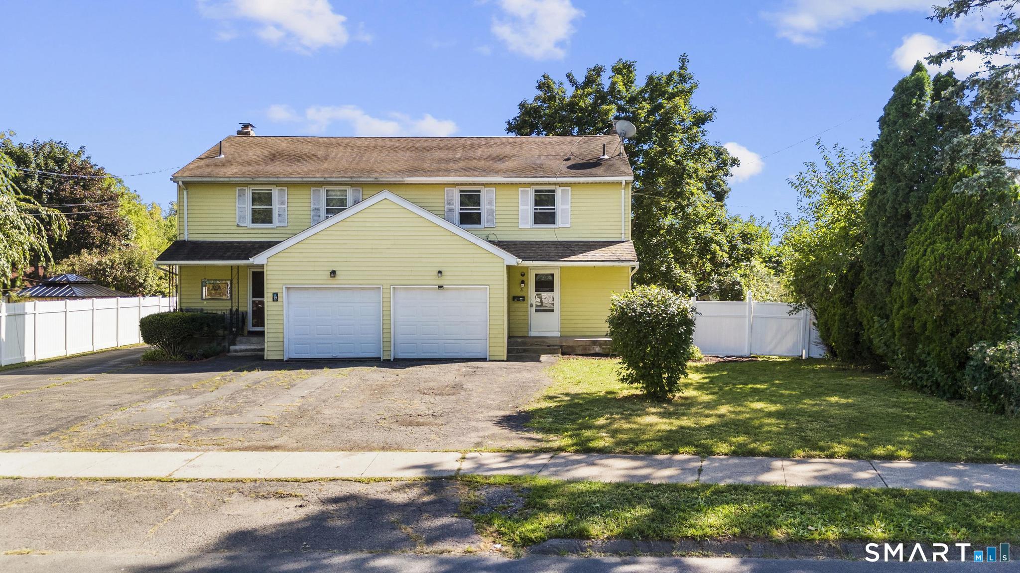 Pale yellow two-story house with an attached double garage, broad driveway, and white side fencing.
