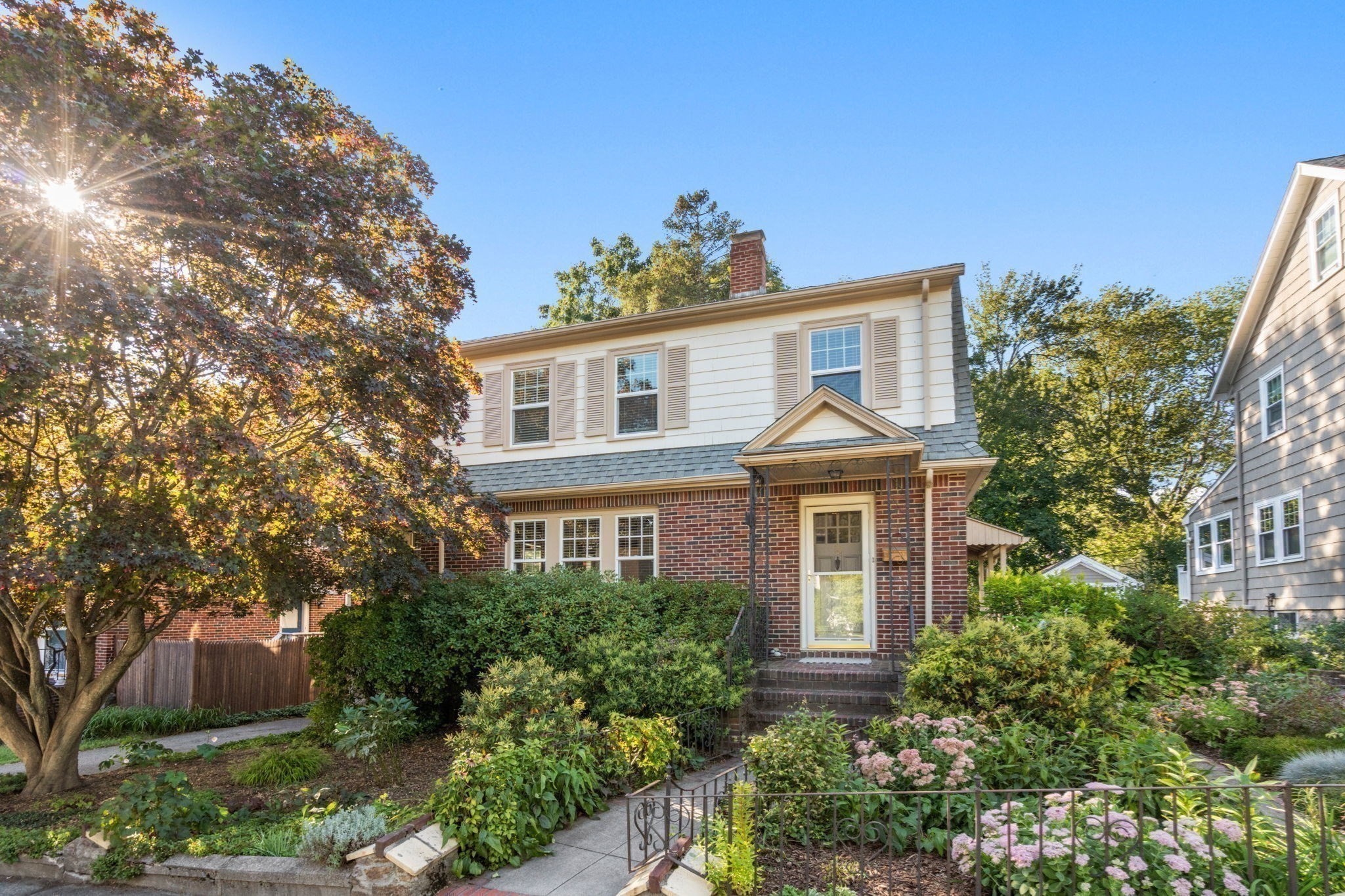 Two-story brick-and-siding house with a landscaped garden and flowering shrubs.