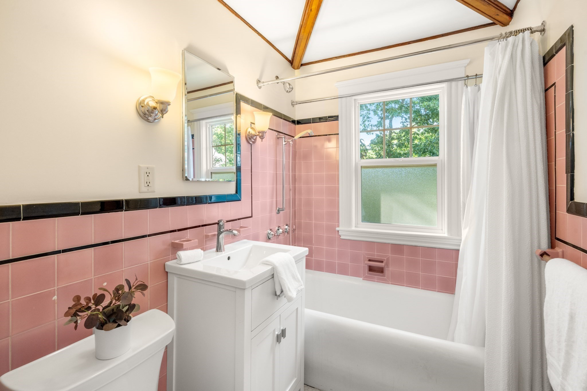 Bathroom with pink tile, a white bathtub, and exposed wood ceiling beams.