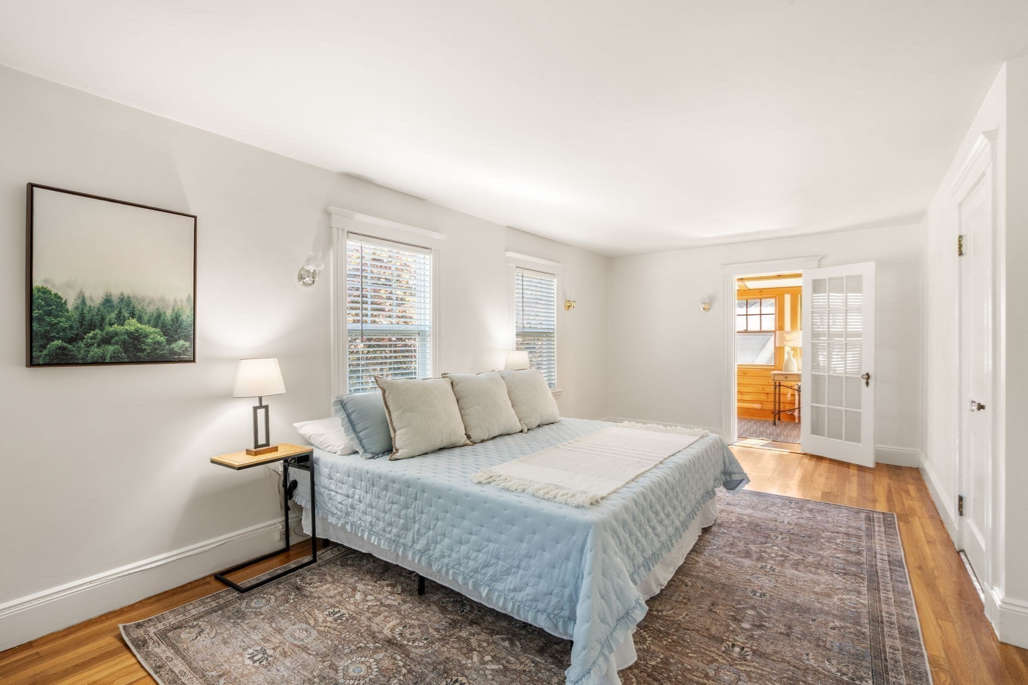 Bright bedroom with a pale blue bed, shuttered windows, hardwood floors, and an open French door.