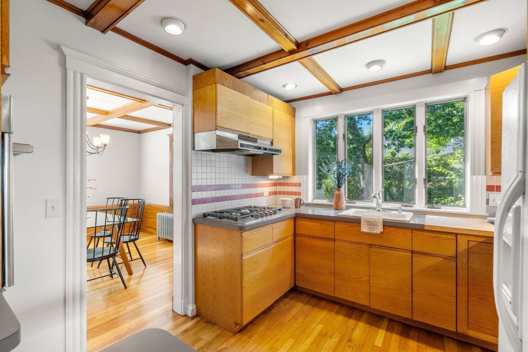 Kitchen with warm wood cabinetry, a beamed ceiling, and a sink beneath wide windows.