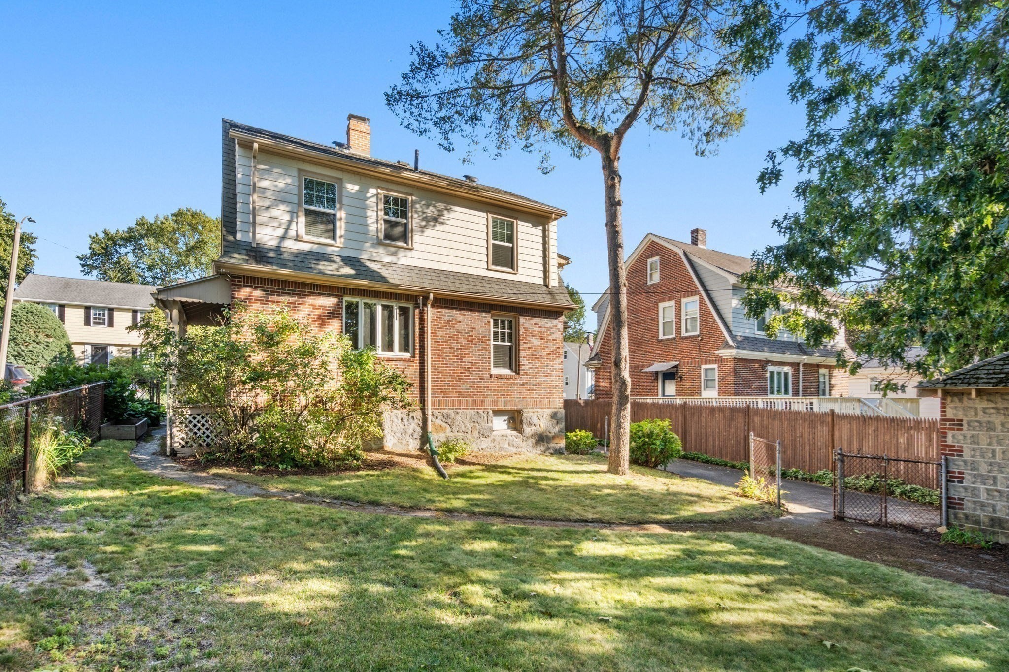 Rear of a two-story brick and siding house beside a grassy yard and mature trees.