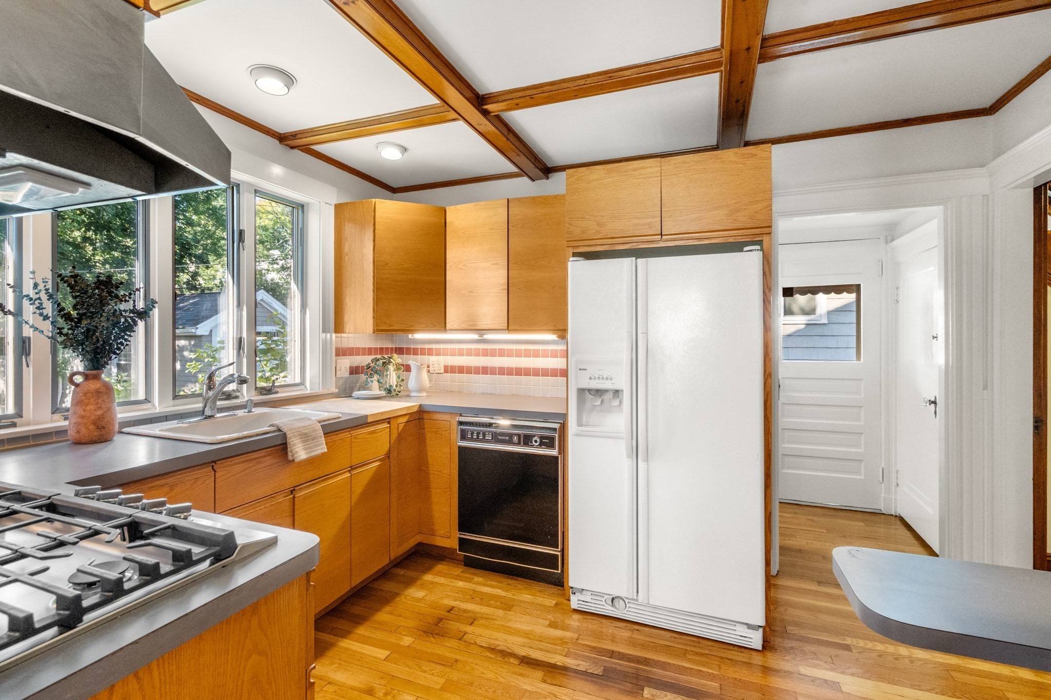 Kitchen with honey-colored wood cabinetry, a coffered ceiling, and large windows above the sink.