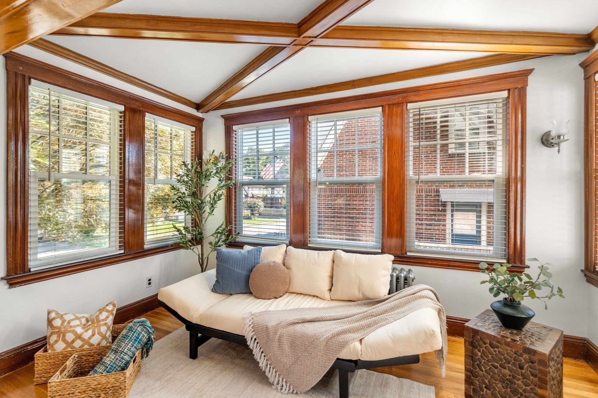 Bright sitting room with a cream sofa, broad windows, and exposed wood ceiling beams.