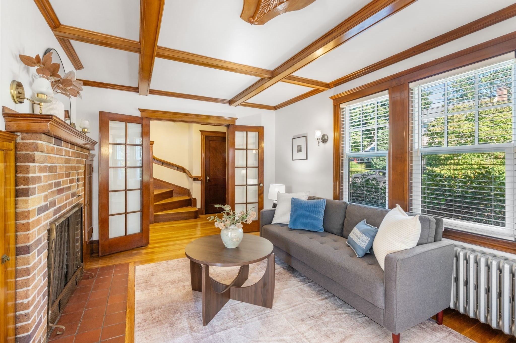 Living room with a brick fireplace, coffered wood ceiling, gray sofa, and glass-paneled doors.