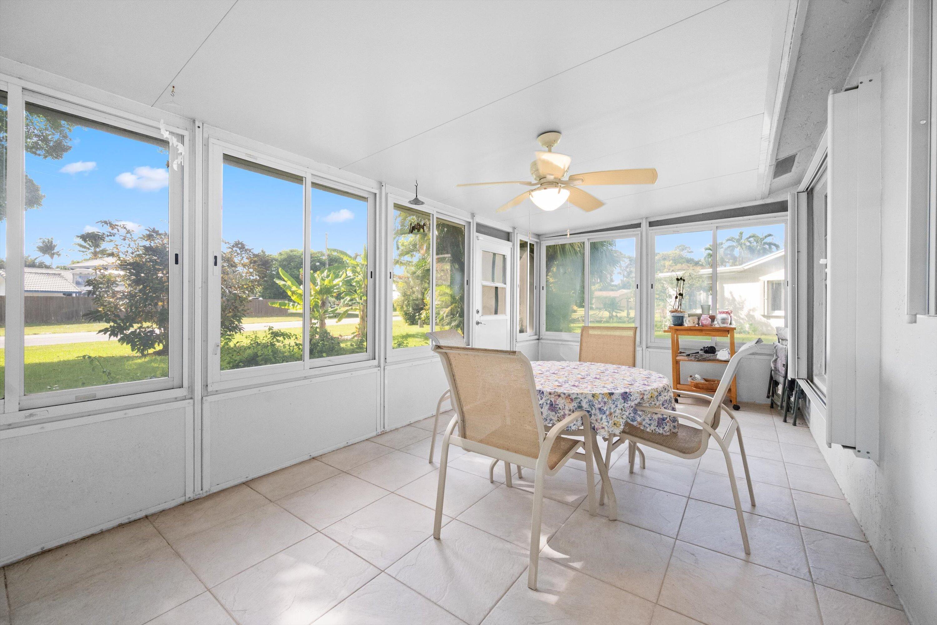 Enclosed sunroom with wraparound windows, tiled floor, ceiling fan, and round dining table.