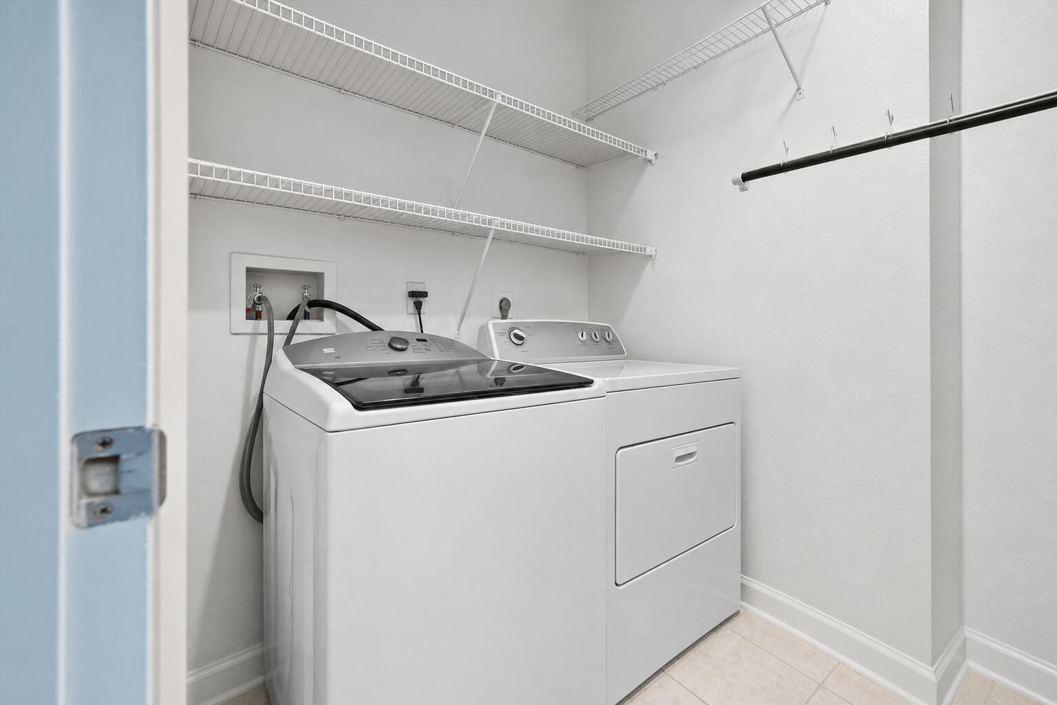 Laundry room with a white washer and dryer, wire shelves, and a hanging rod.