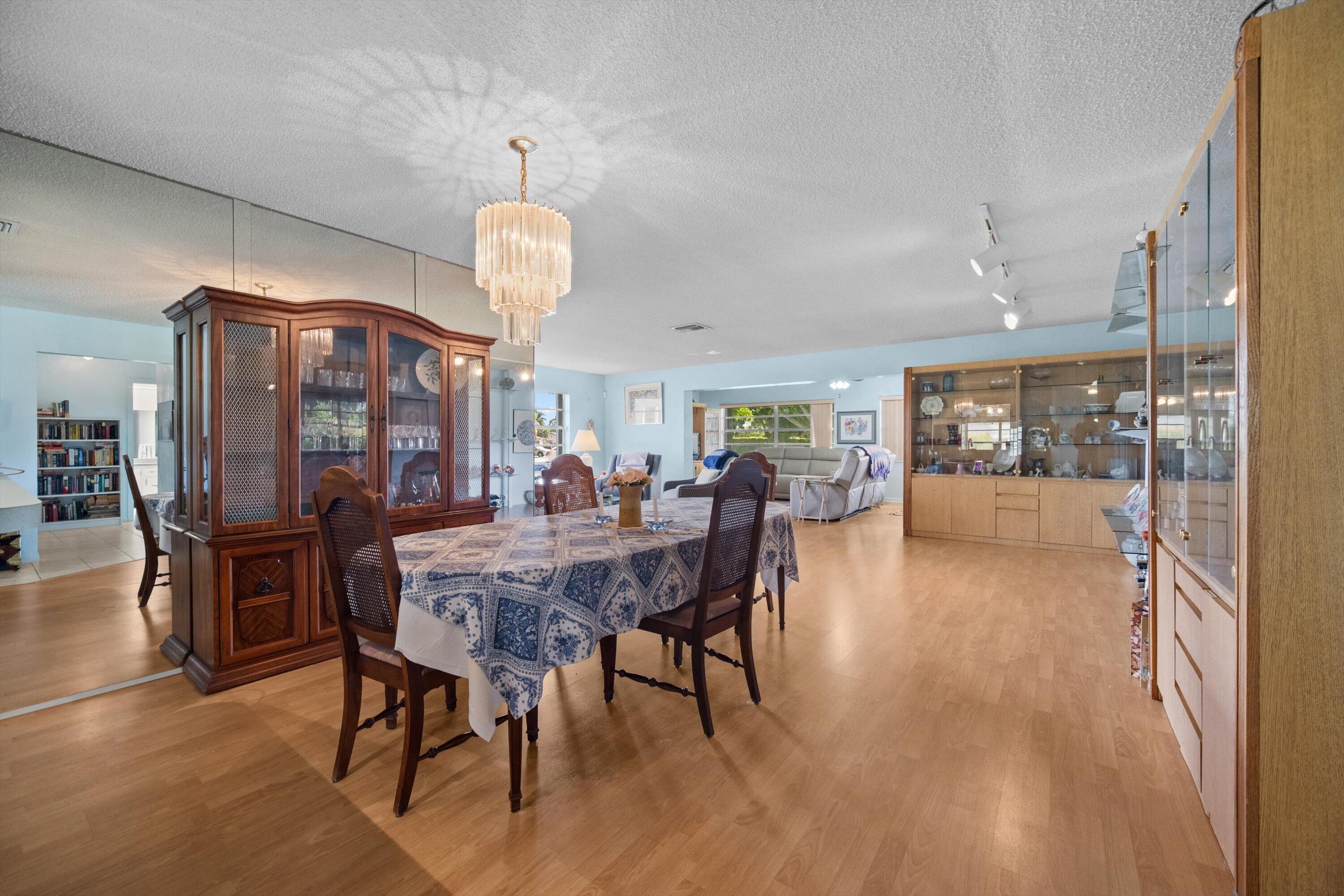 Dining room with a patterned tablecloth, dark wood cabinets, and a chandelier, opening to the living area.