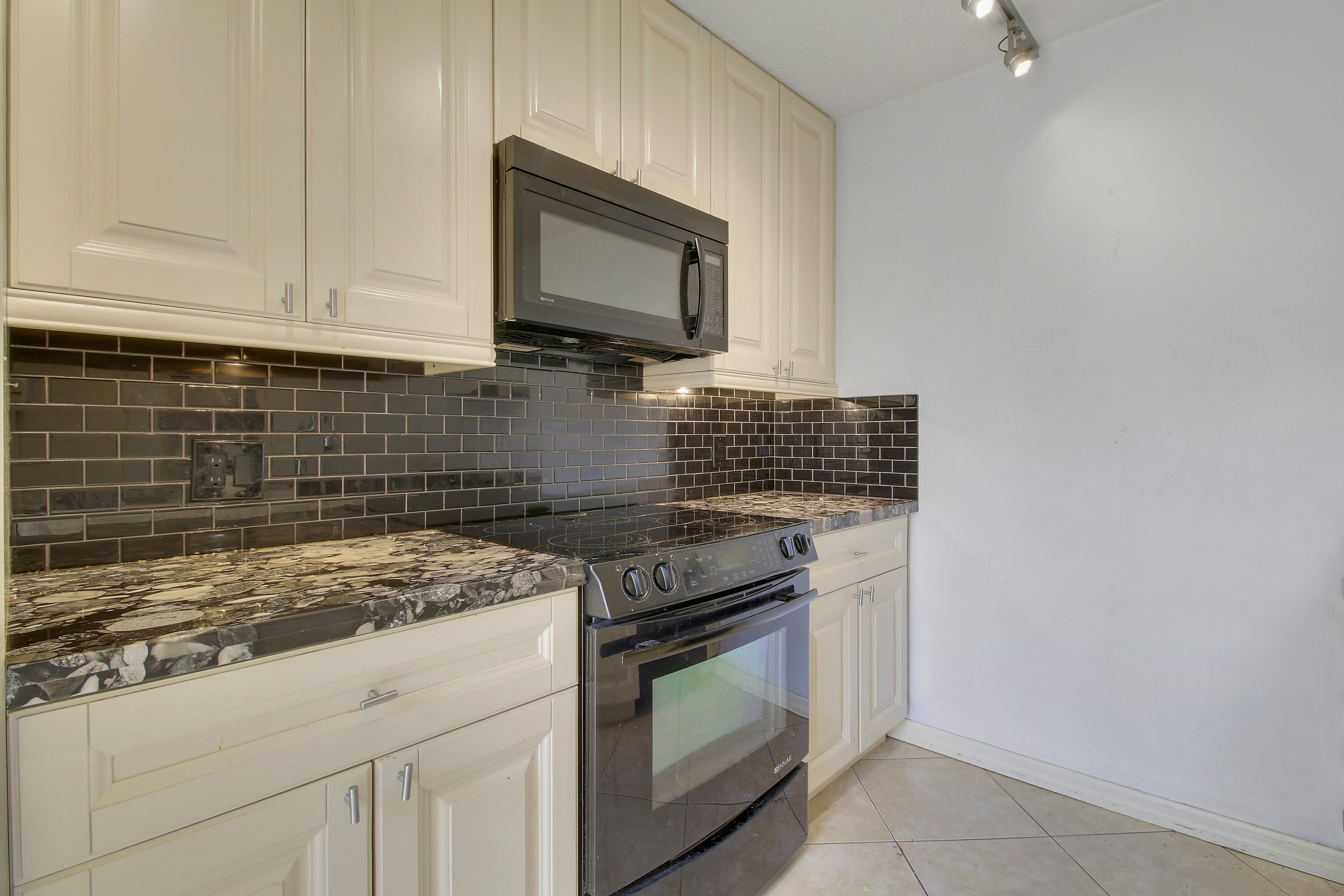 Kitchen with cream cabinets, dark tile backsplash, patterned stone counters, and stainless steel appliances.