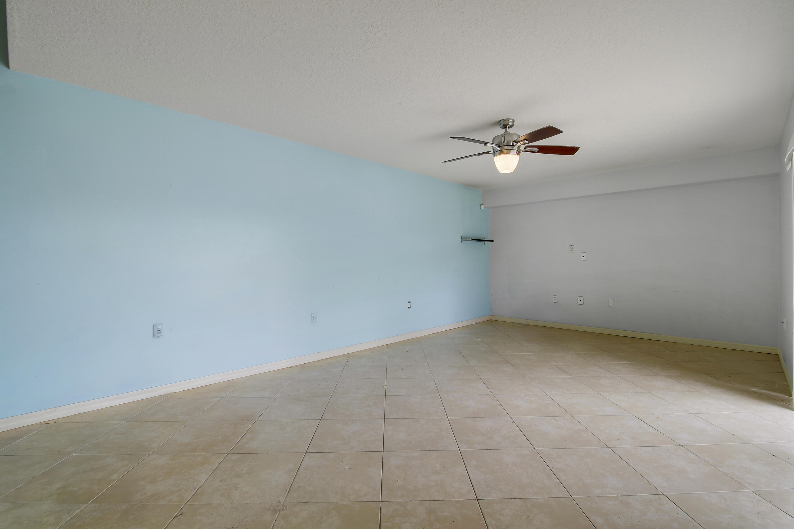 Vacant room with pale blue walls, tan tile floors, and a ceiling fan with a light.