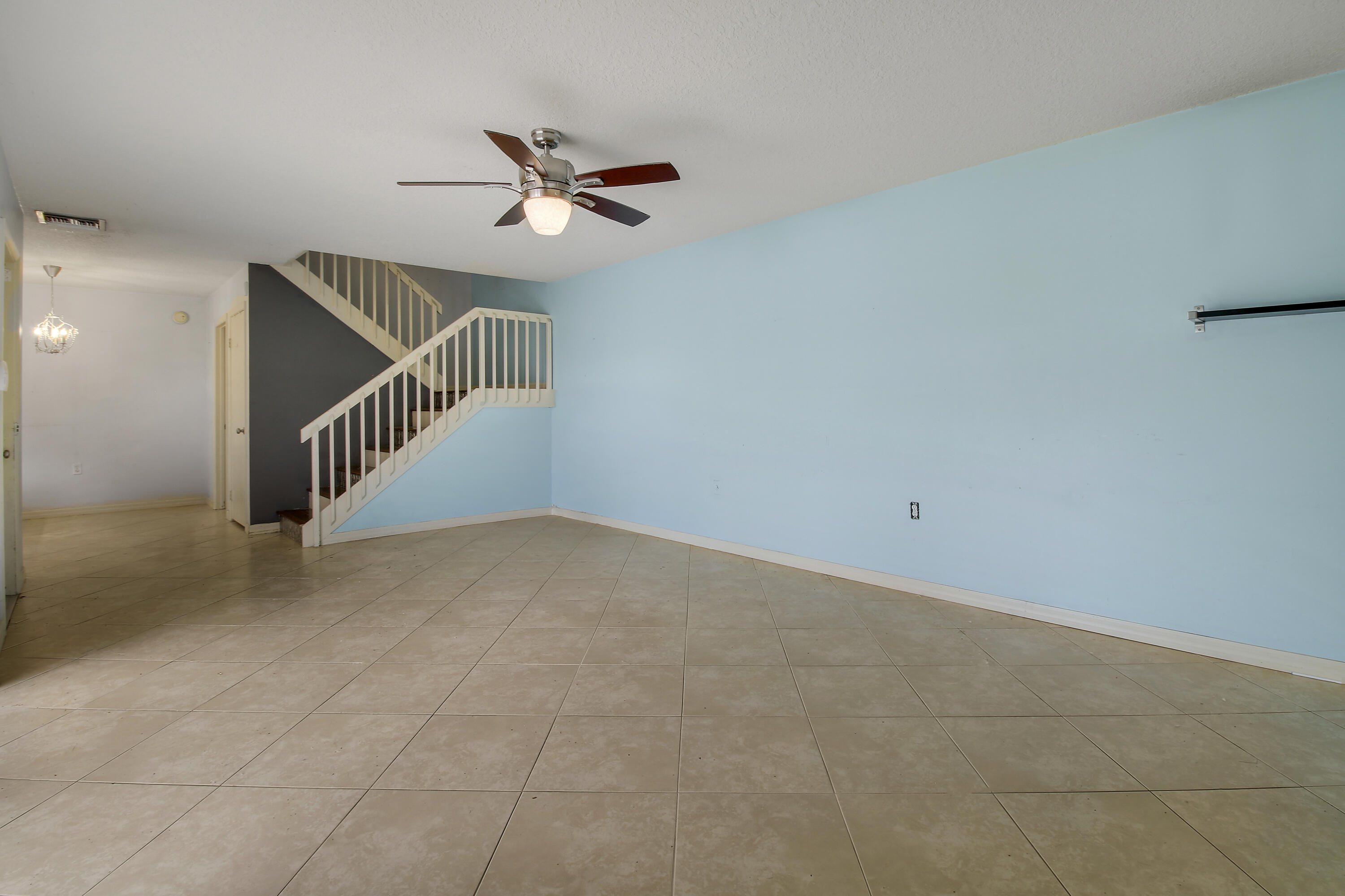 Empty living area with tiled floors, blue walls, and a staircase with white railing.