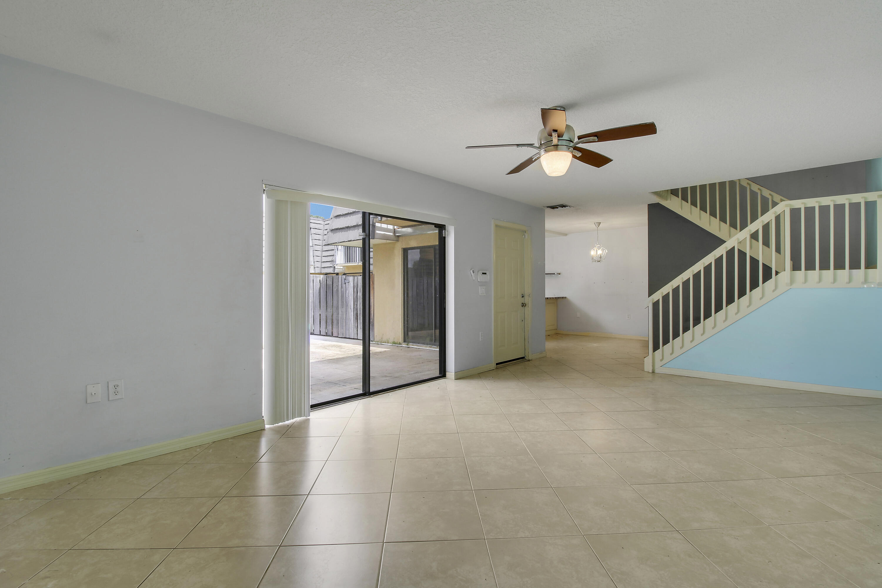 Vacant living room with tiled floors, a sliding patio door, and a staircase with white railings.