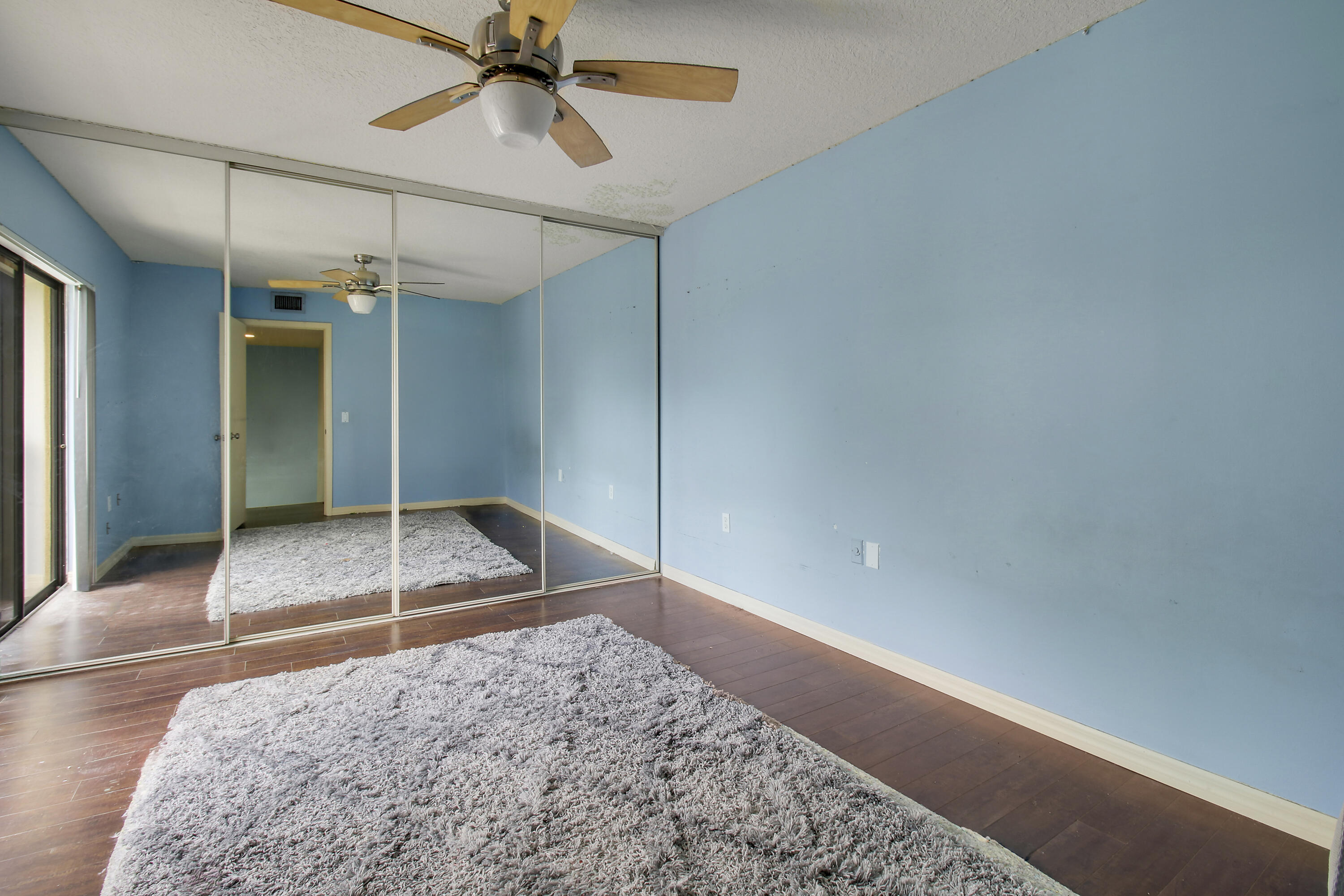 Empty blue bedroom with mirrored closet doors, dark flooring, and gray shag rugs.