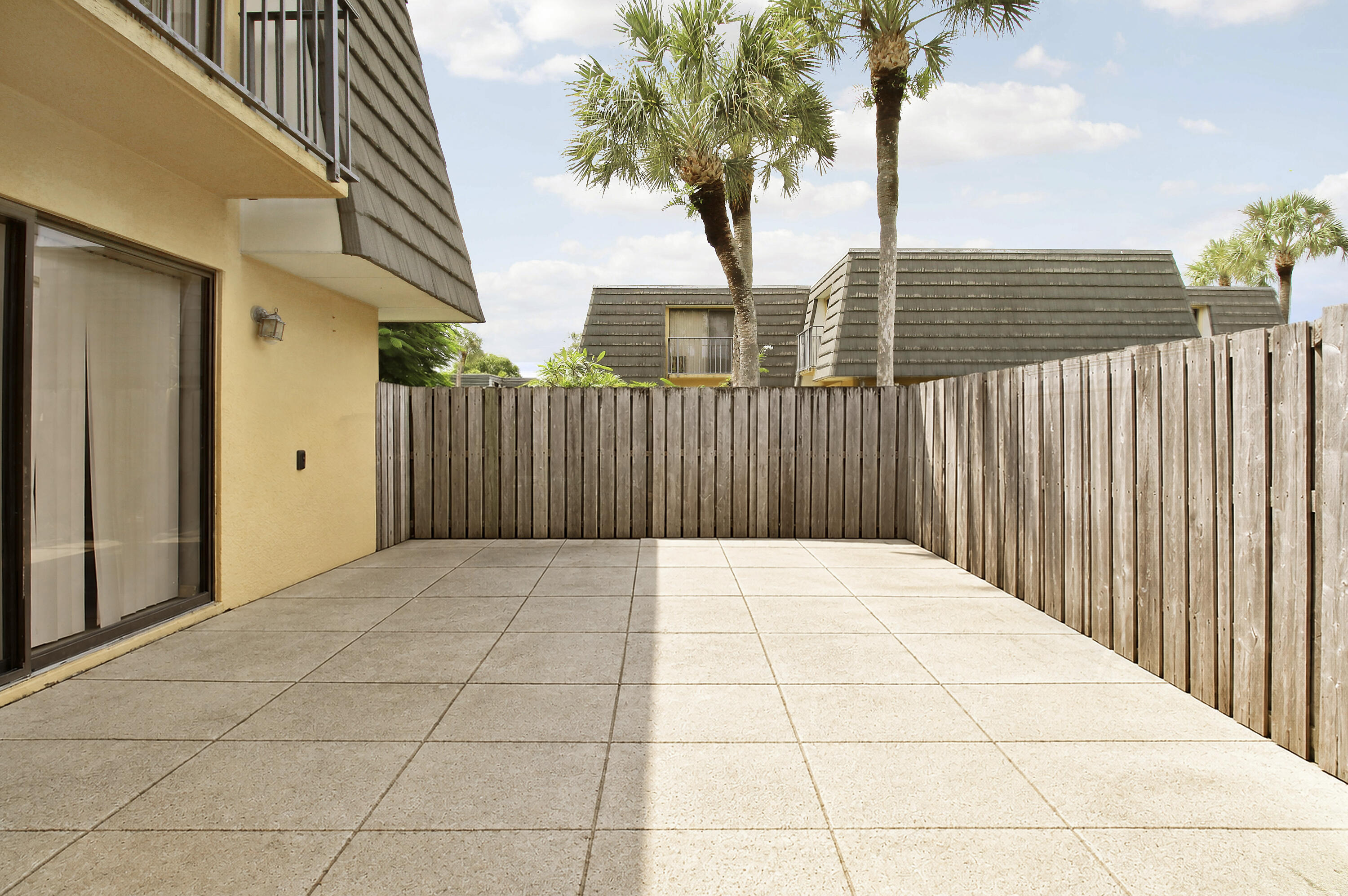 Paved patio enclosed by a wooden privacy fence, beside a yellow stucco home with a sliding glass door.