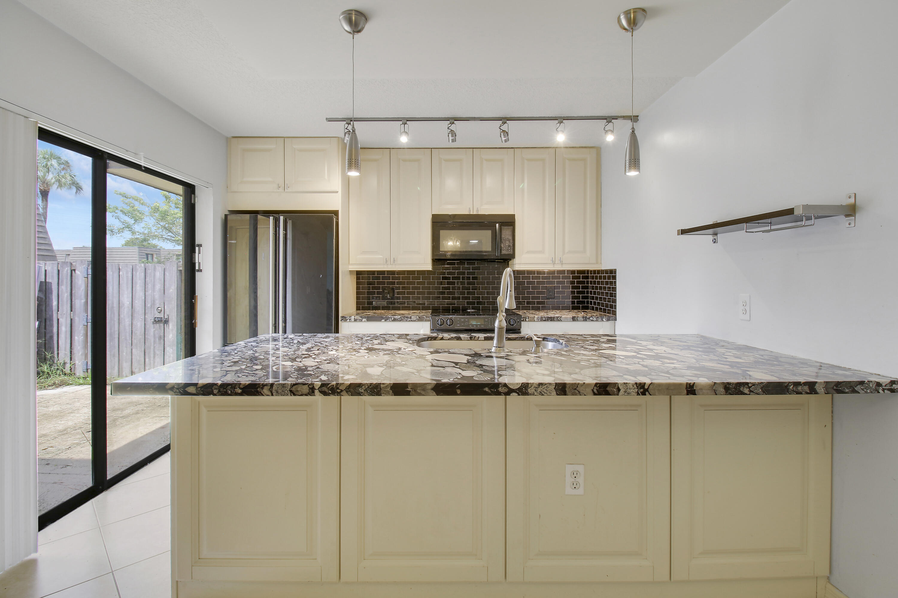 Kitchen with a large stone island, cream cabinets, dark tile backsplash, and sliding glass door to a patio.
