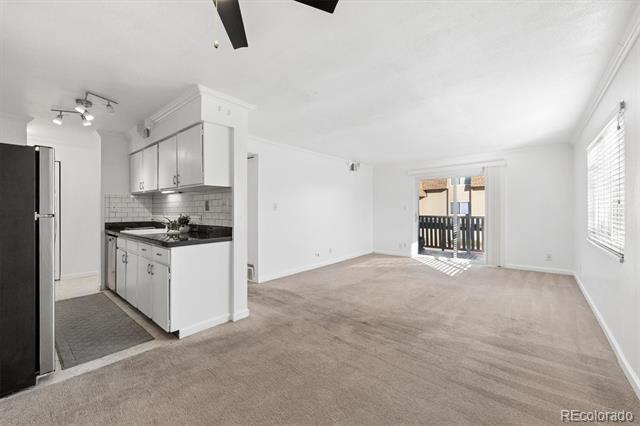 Open living room with adjoining white kitchen, carpeted floor, and sliding glass door to balcony.