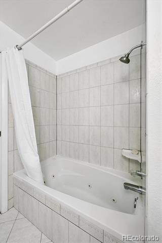 Bathroom with a white bathtub, tiled surround, shower curtain, and glass shower panel.