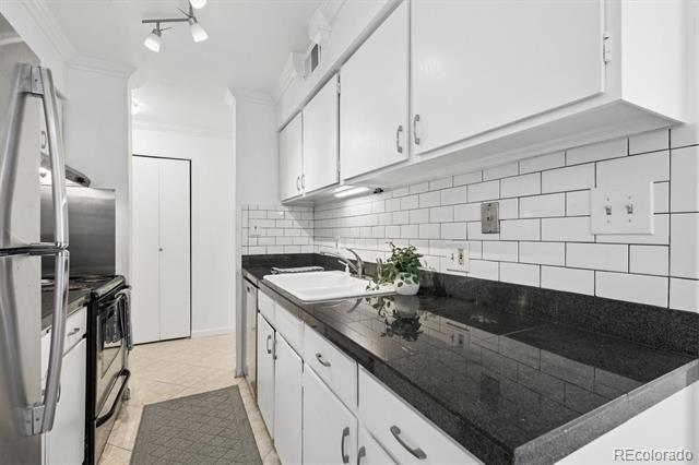 Narrow kitchen with white cabinets, dark granite counters, subway tile backsplash, and stainless steel appliances.