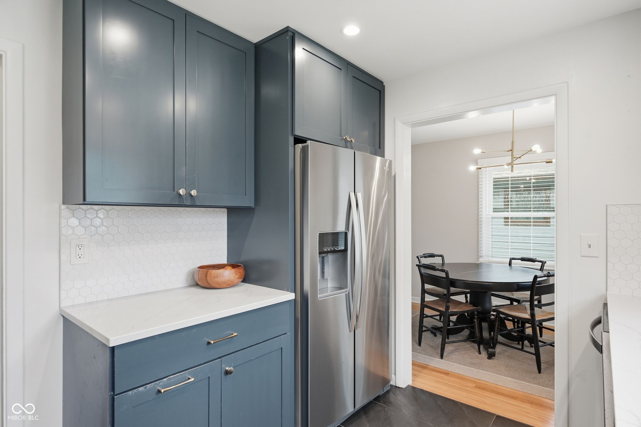 Kitchen with blue-gray cabinets and hexagonal tile backsplash, opening to a dining room with a round table.