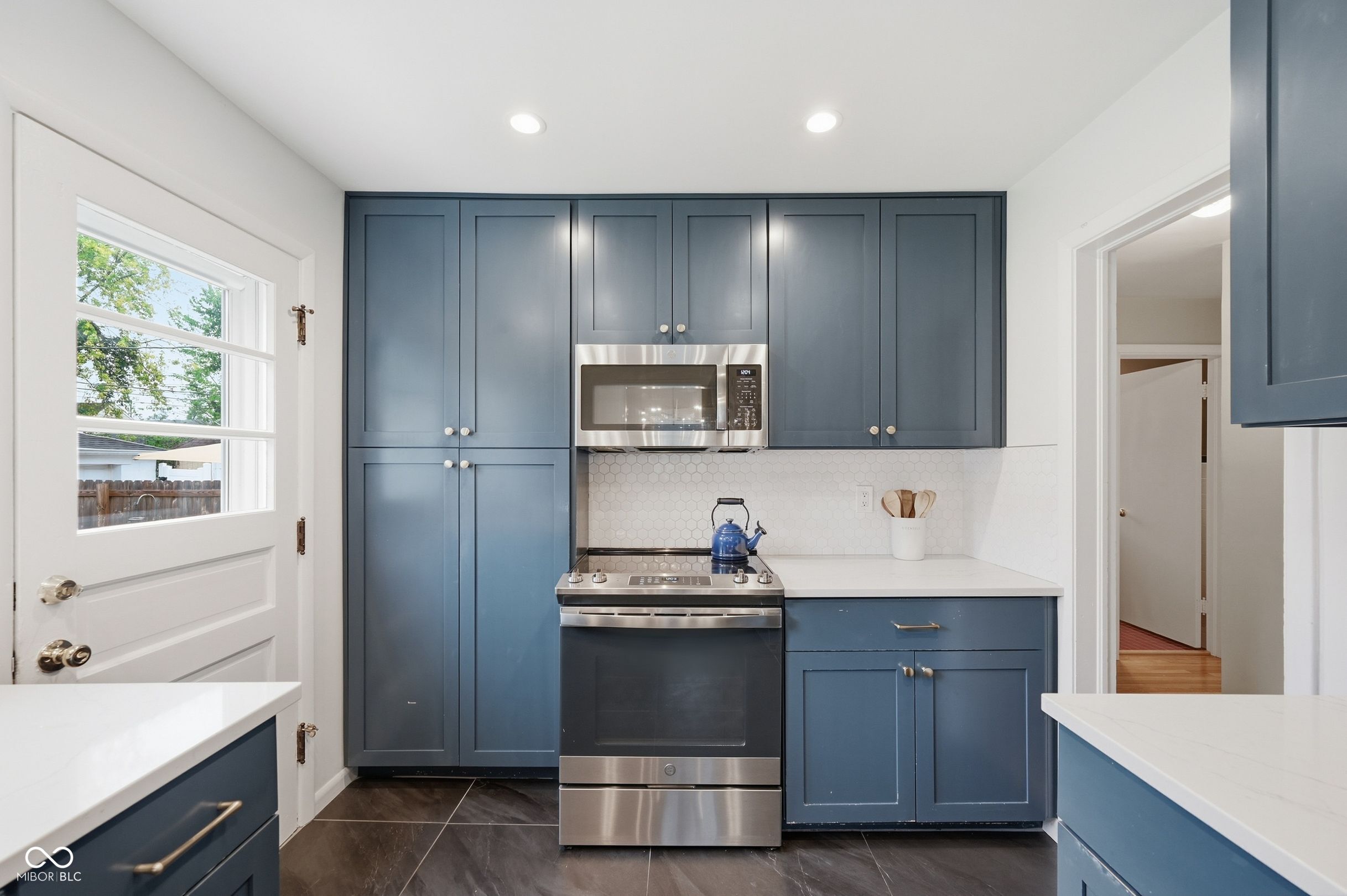 Kitchen with navy cabinets, white countertops, hexagonal tile backsplash, and stainless steel appliances.