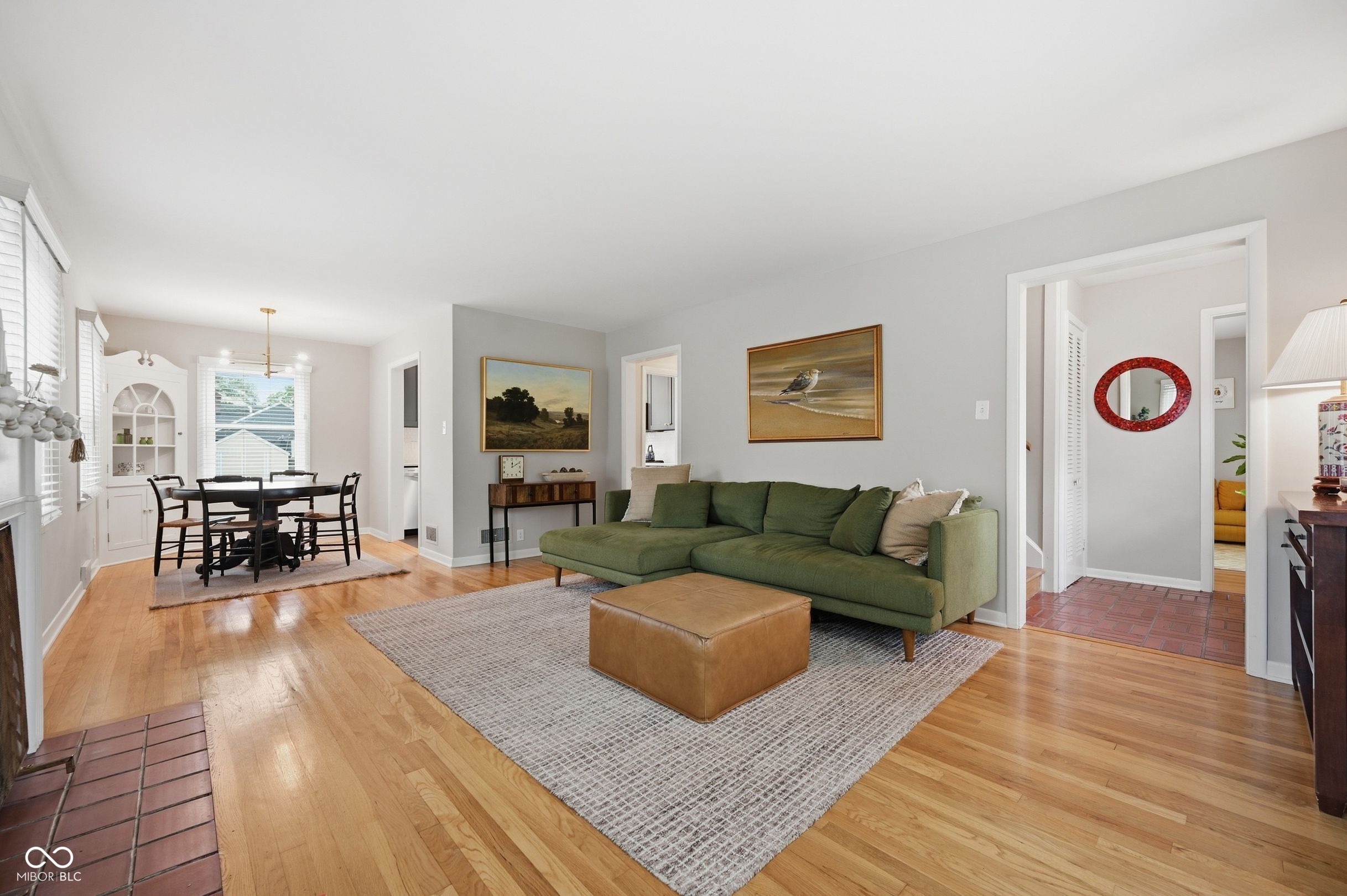 Living and dining area with a green sectional, hardwood floors, and a tiled entryway.