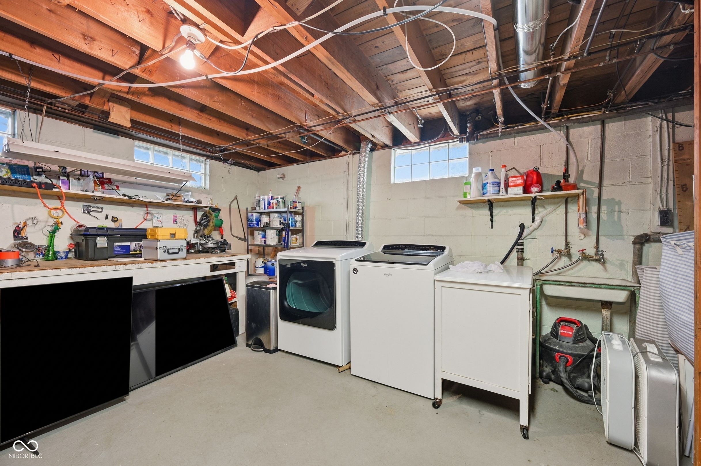Basement laundry room with washer, dryer, utility sink, and exposed ceiling joists.