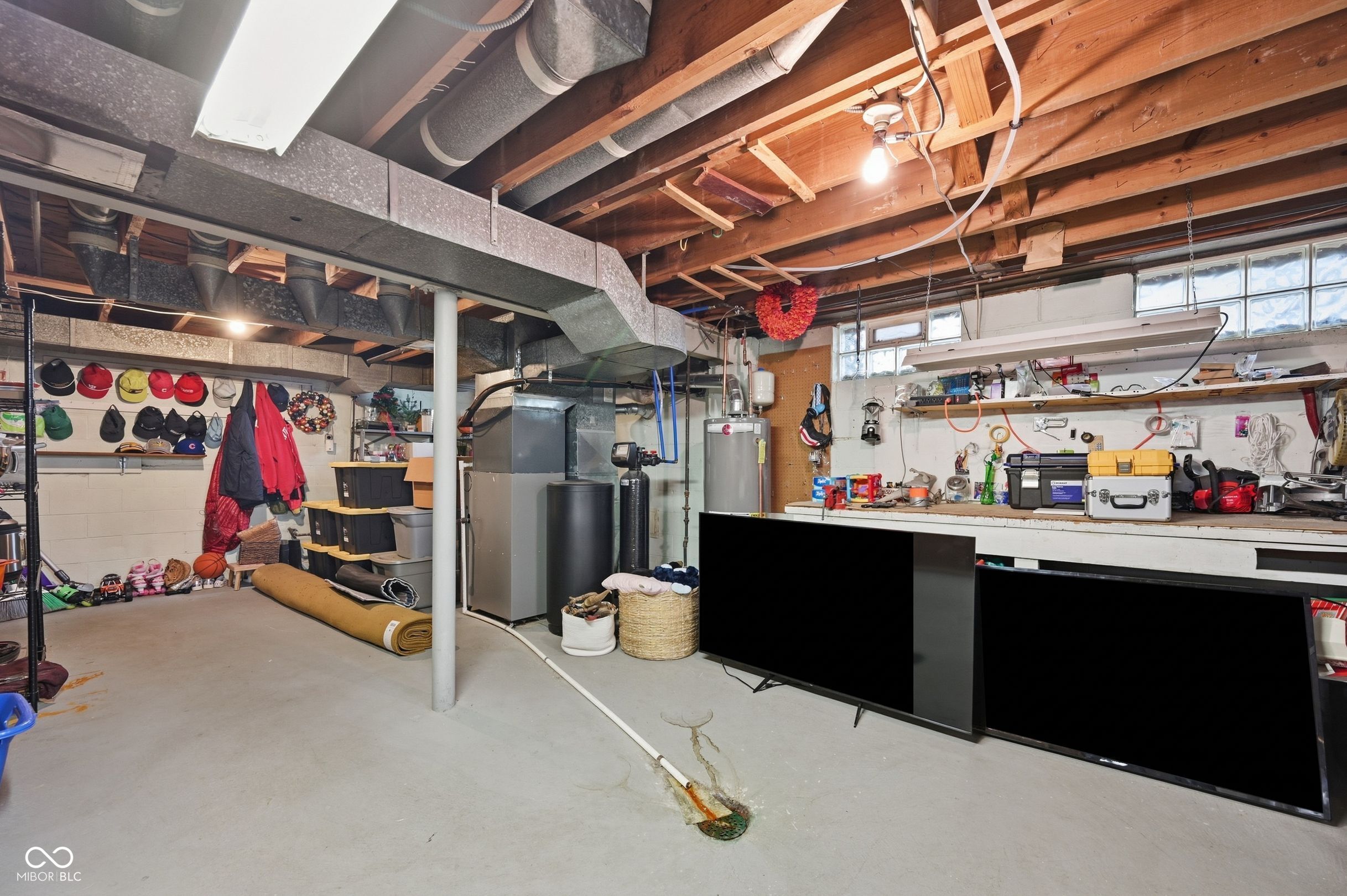 Unfinished basement with exposed ductwork, a water heater, storage shelves, and household belongings.