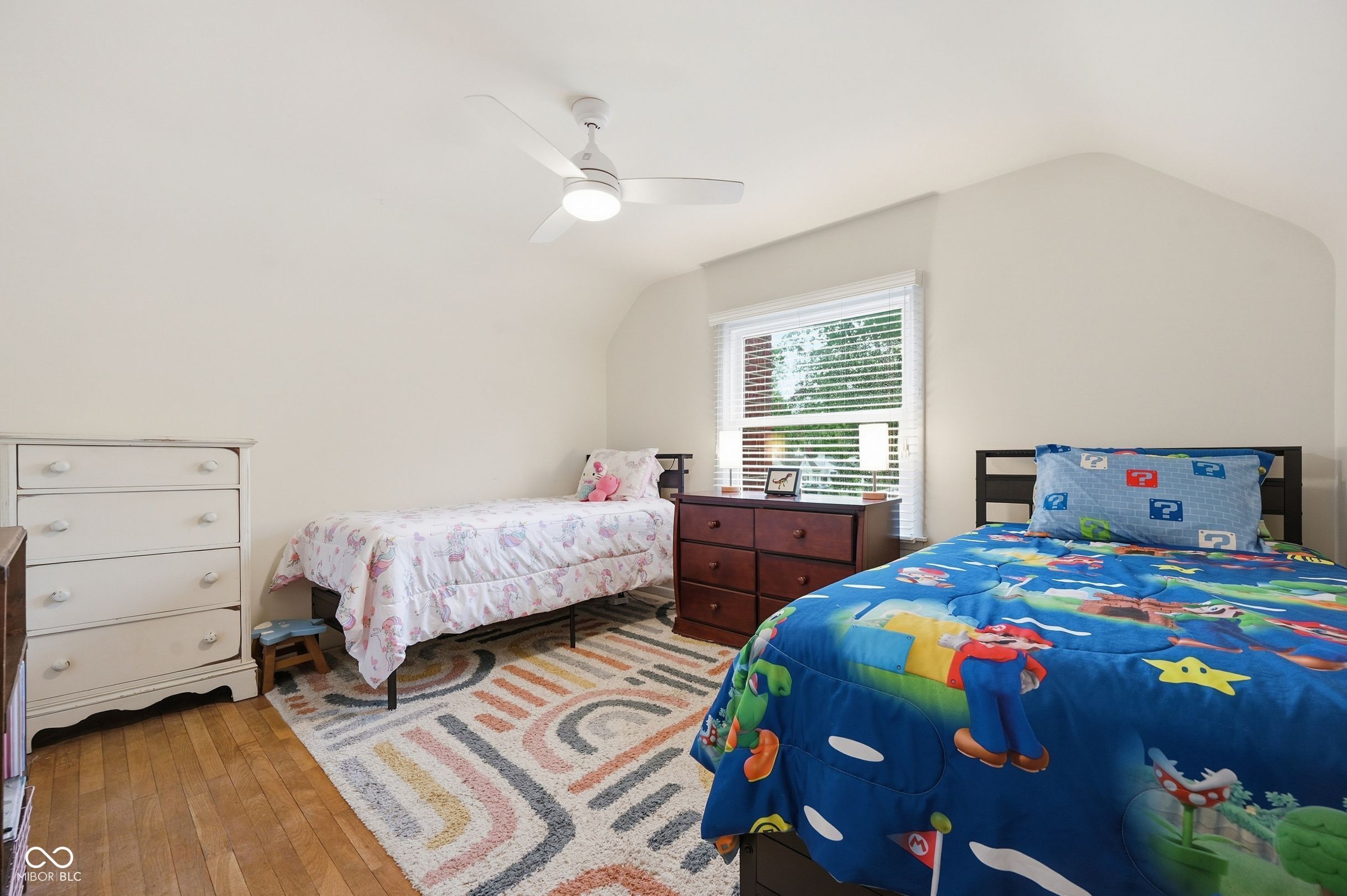 Bedroom with two single beds, colorful bedding, a dresser, and a patterned rug.
