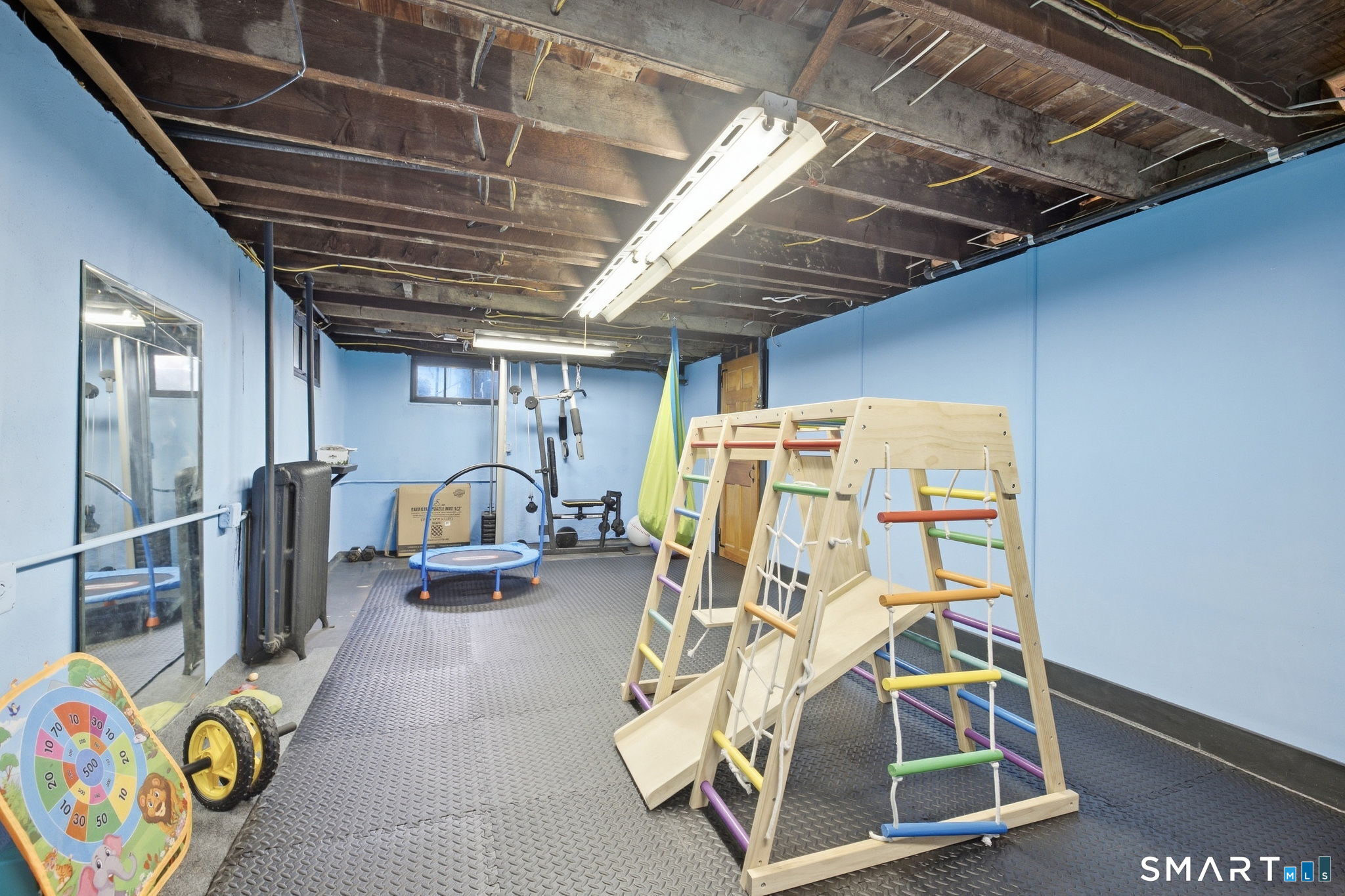 Indoor playroom with a wooden climbing gym, slide, and small trampoline.