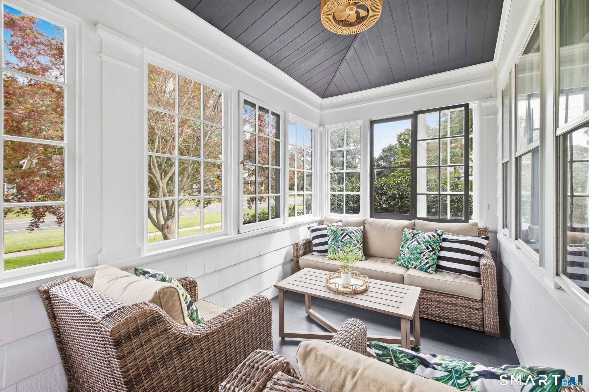 Furnished sunroom with wicker seating, wraparound windows, and a dark vaulted ceiling.